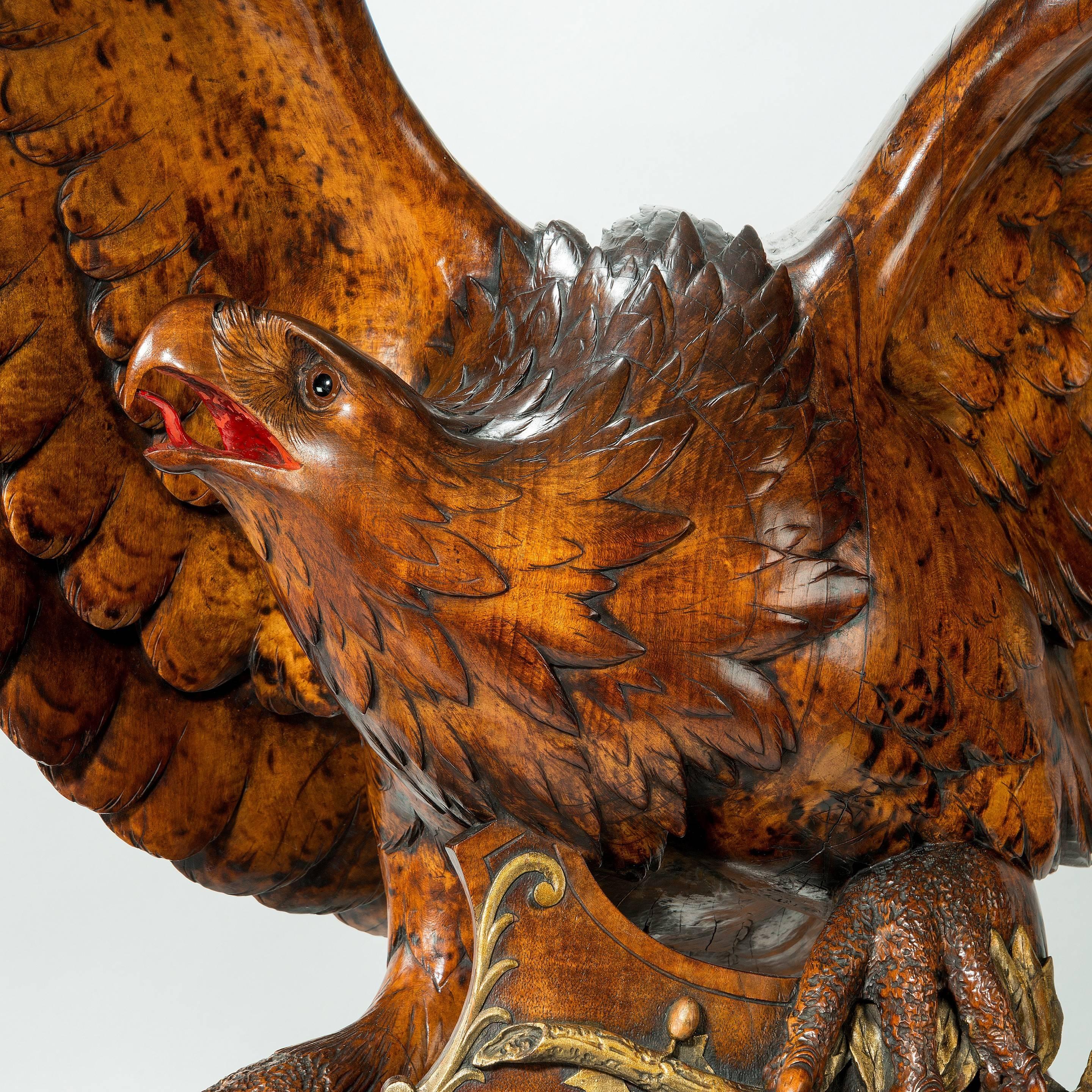 A monumental and striking ‘Black Forest’ walnut carving of an eagle perched on a toppled shield, E Binder, Shown with outstretched wings and the head turned to the right , the talons gripping a sheaf of arrows and a shield decorated in gilt with 12