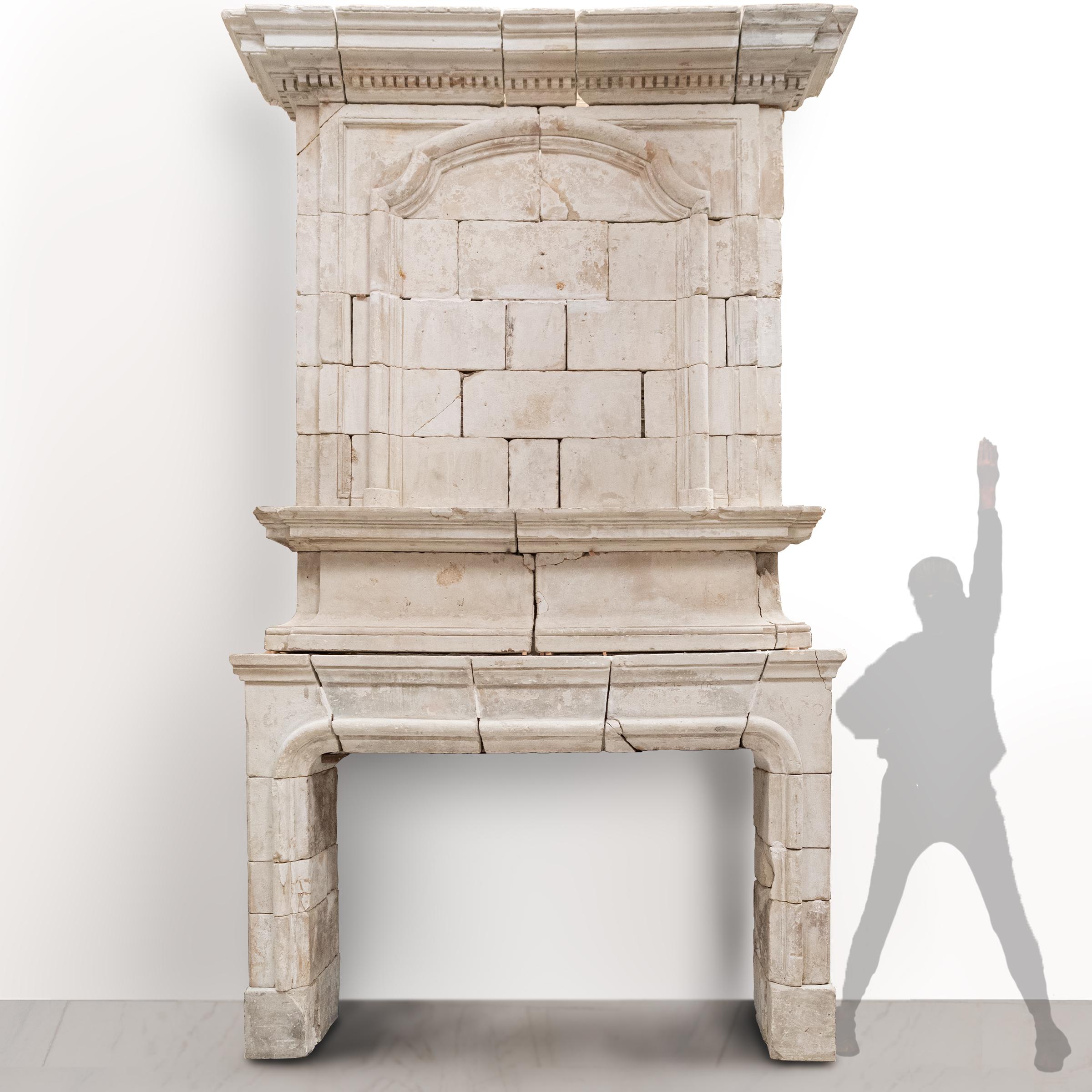 An original French early 18th Century Antique stone fire surround. 

Of significant height, this magnificent period piece is composed of blocks of pale honey-coloured French stone and has a striking trumeau that is surmounted by a stepped and