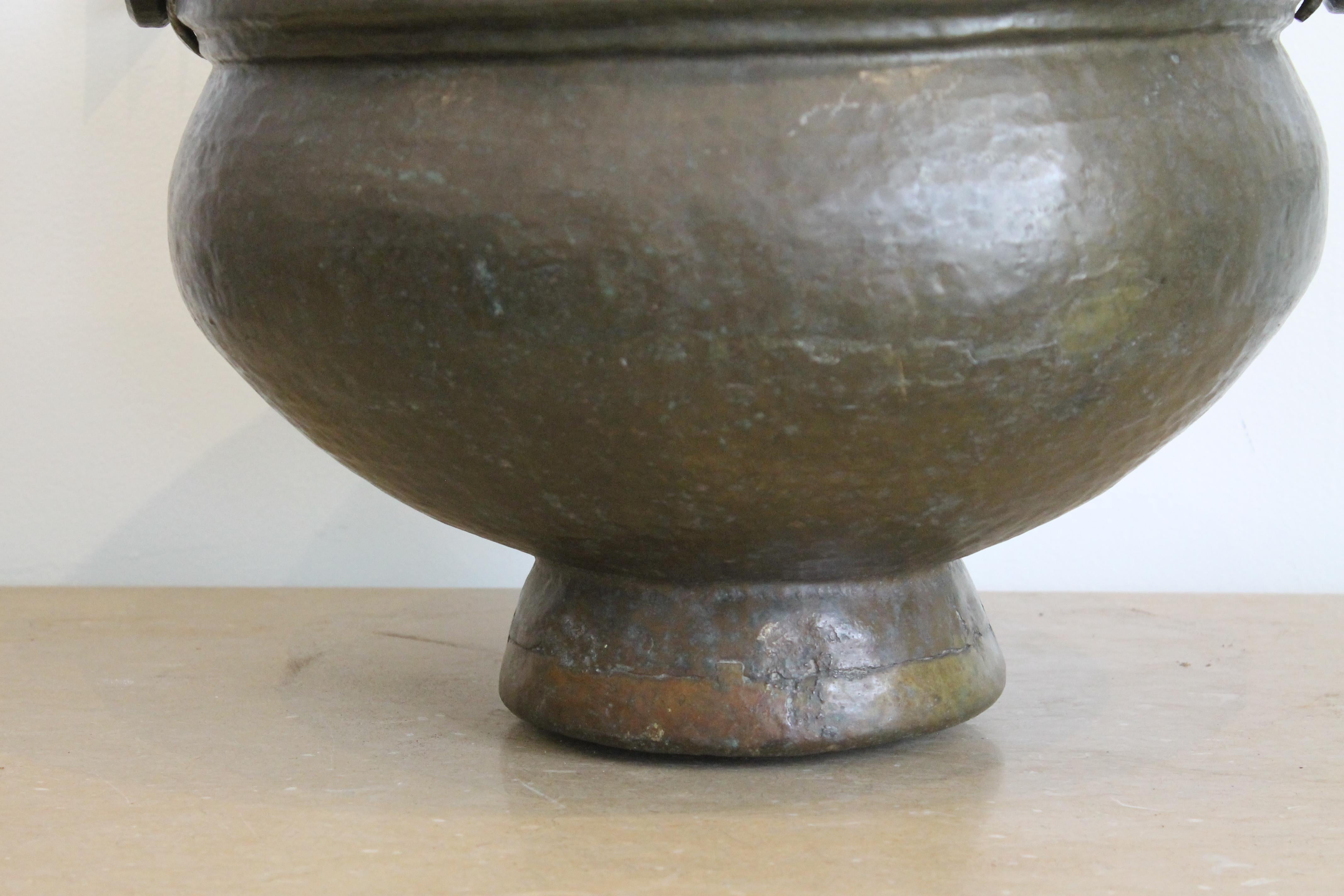 A large hammered brass pot with forged brass ring handles, and dove-tail type construction at the base. Two stamped markings are done in the English manner, both incomplete and illegible. Heavy gauge brass with old patina. Pot measures 13.5
