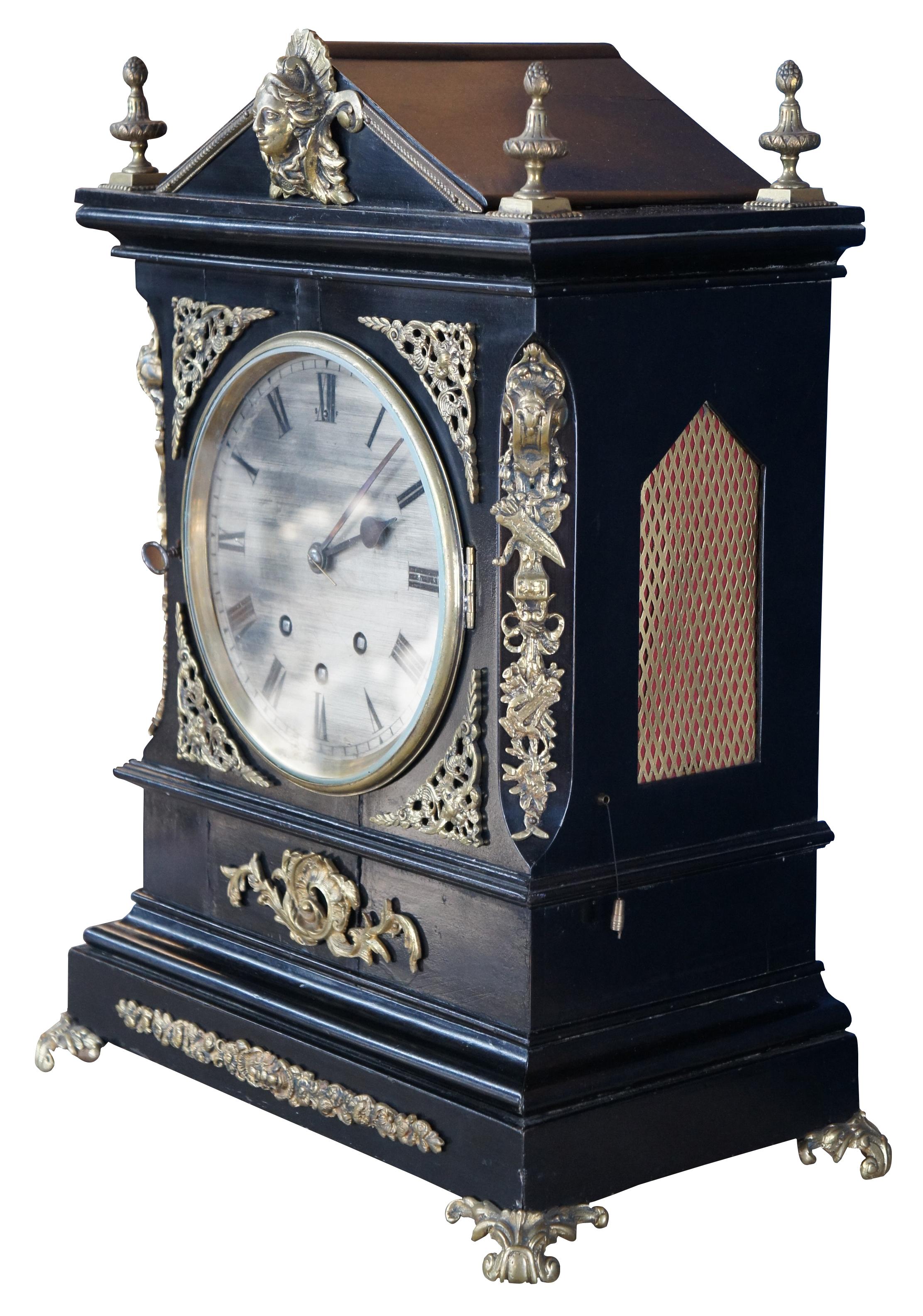 Antique English Georgian bracket clock featuring ebonized case with ormolu accents. The ornate case features gothic styling with an arched top, mesh gilt side panels, jardiniere urn shaped finials and figural mount. Chimes beautifully with several