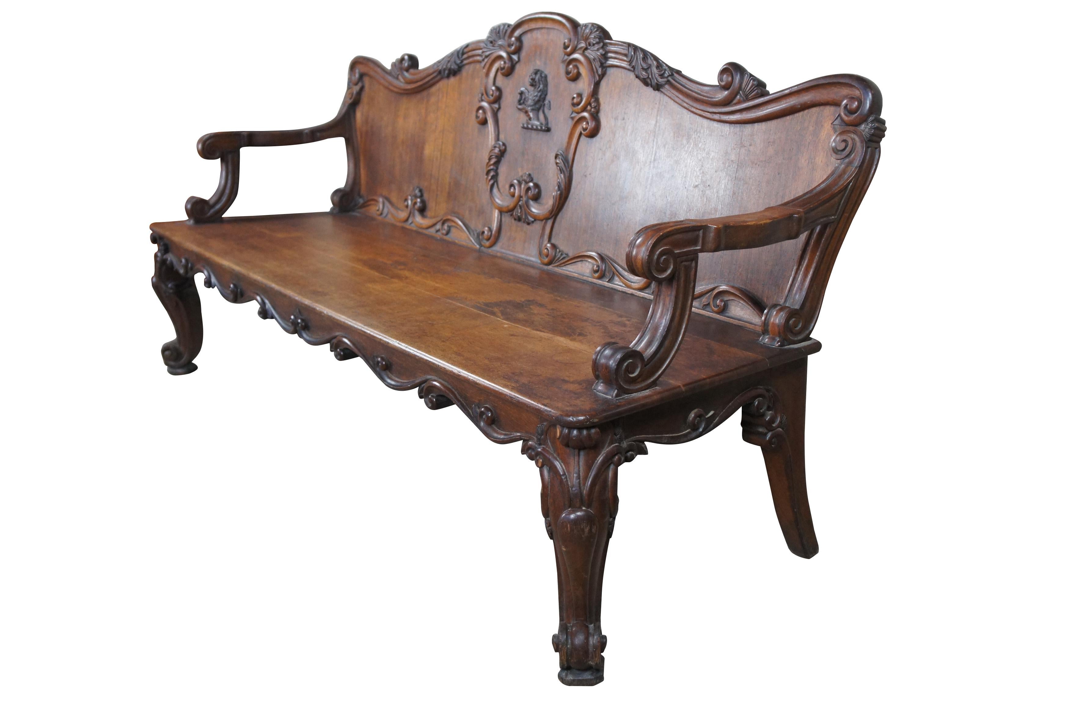 A rare and impressive hall bench / settle from Moreton Hall in Lancashire United Kingdom, circa 1830s.  Made of oak featuring serpentine hand carved form with lion passant holding an acorn, heavy acanthus leaf foliate and swags. The bench showcases