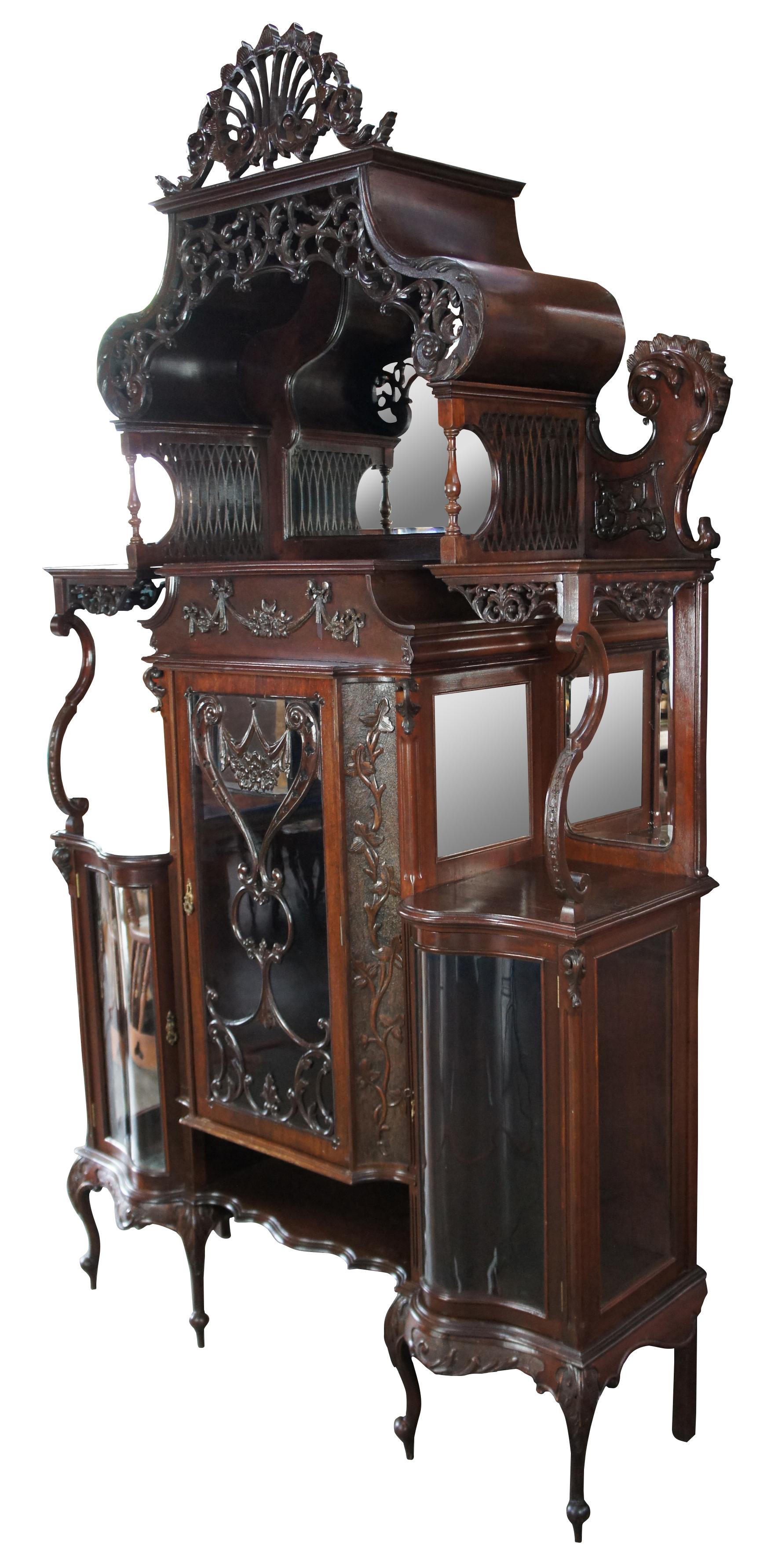 A one of a kind antique Late Victorian English etagere curio display cabinet. Made from carved mahogany featuring ornate serpentine form with Neoclassical carved, pierced and reticulated accents, beveled mirrors, S curve glass and cabriole legs.