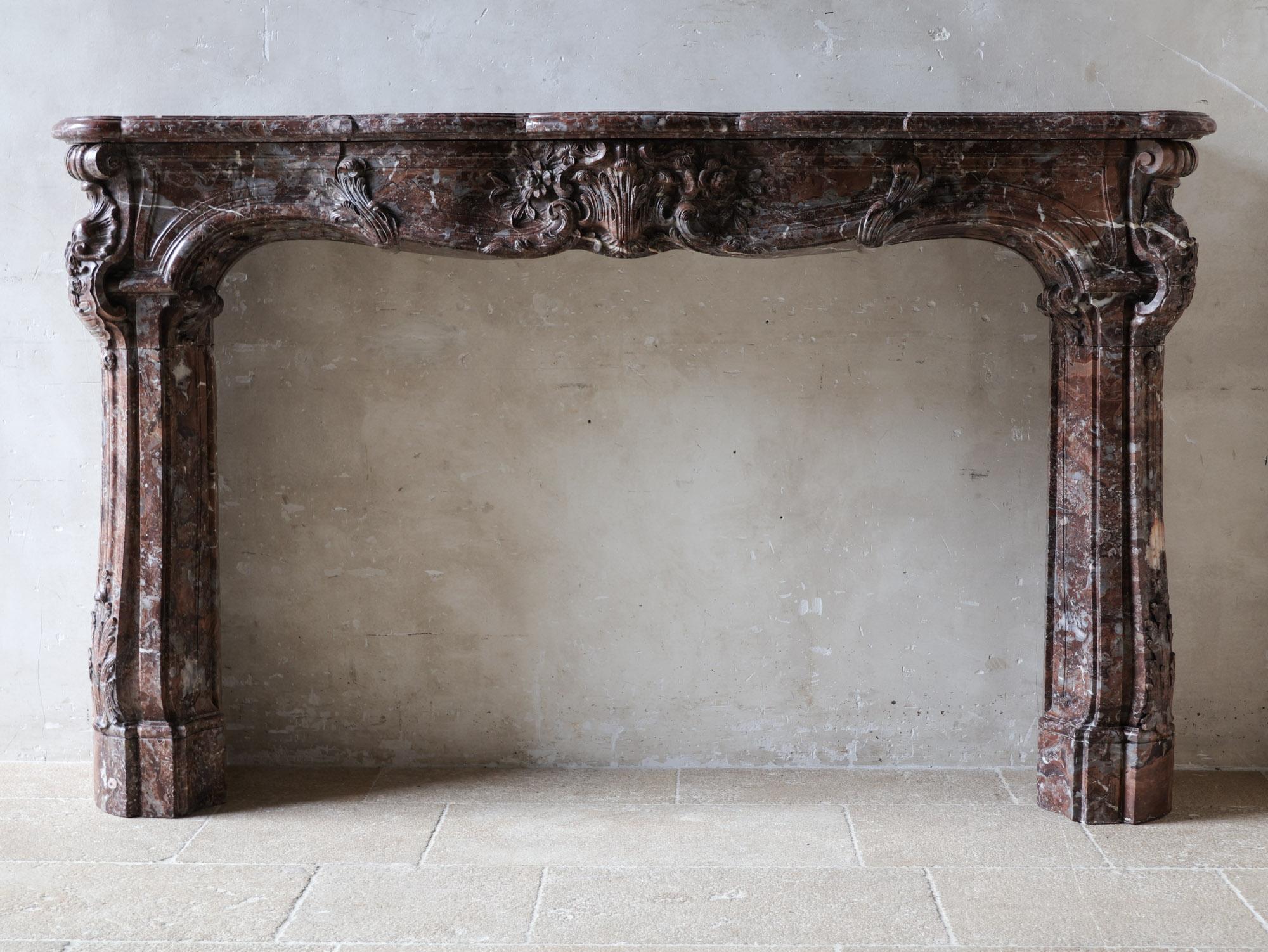 Esta monumental chimenea antigua es una pieza rara, elaborada en el elegante estilo Luis XV y fabricada con mármol Rouge Royal excepcionalmente grueso y ricamente veteado. Esta prestigiosa piedra natural destaca por su base de color rojo intenso y