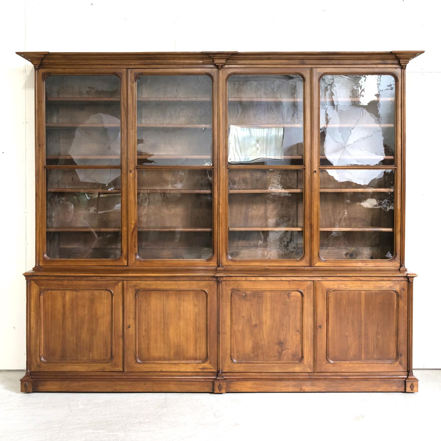 A fine antique French Directoire style bibliothèque handcrafted of beautiful cherry wood by talented artisans in the city of Lyon, circa 1900. The upper bookcase of this grand chateau piece boasts a stepped crown above two pairs of three-quarter