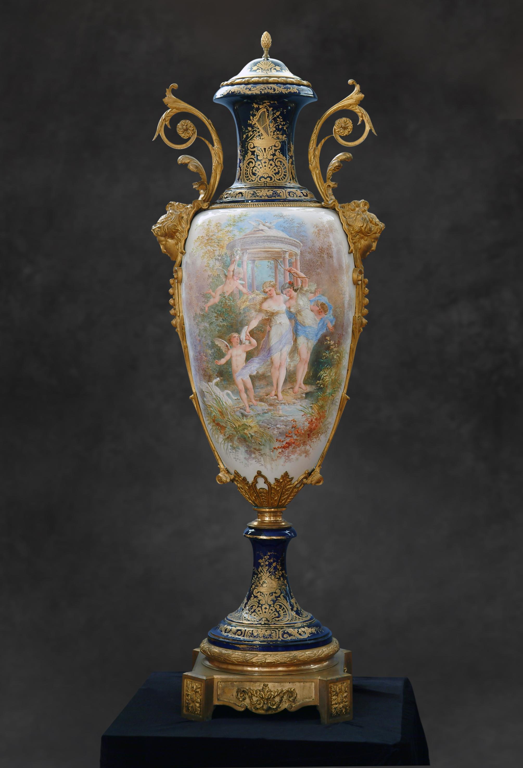 A palace size antique French ormolu-mounted Sevres Porcelain covered Urn. This magnificent vase painted on a white porcelain body centered with a Bouguereau style painting of female beauties encompassed by Cupids in a mythical garden setting with