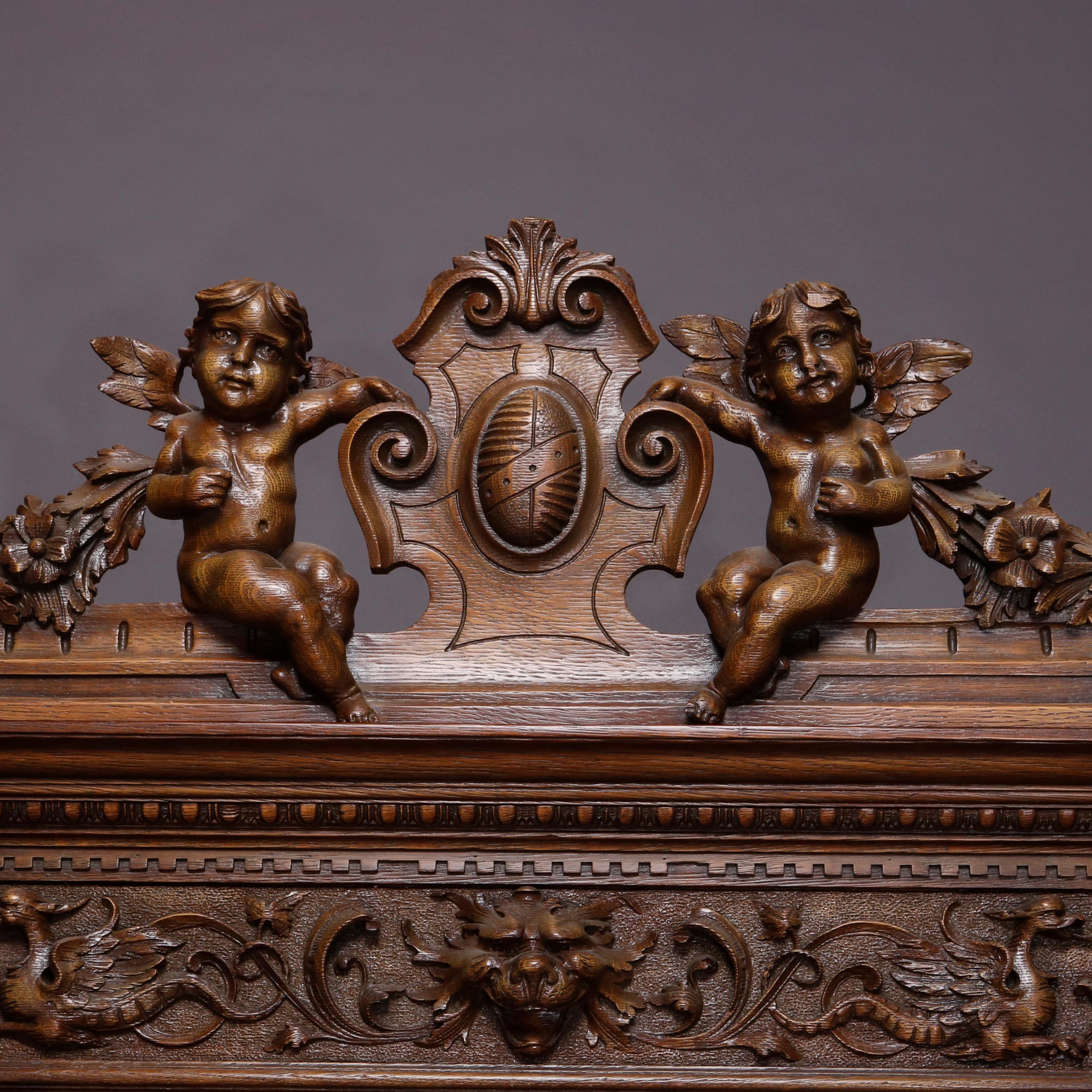 An antique R. J. Horner figural china cabinet of monumental proportion offers oak construction with pierced crest having central shield form cartouche with fleur-de-lis and flanking cherubs surmounting carved cabinet having wind god mask, griffin
