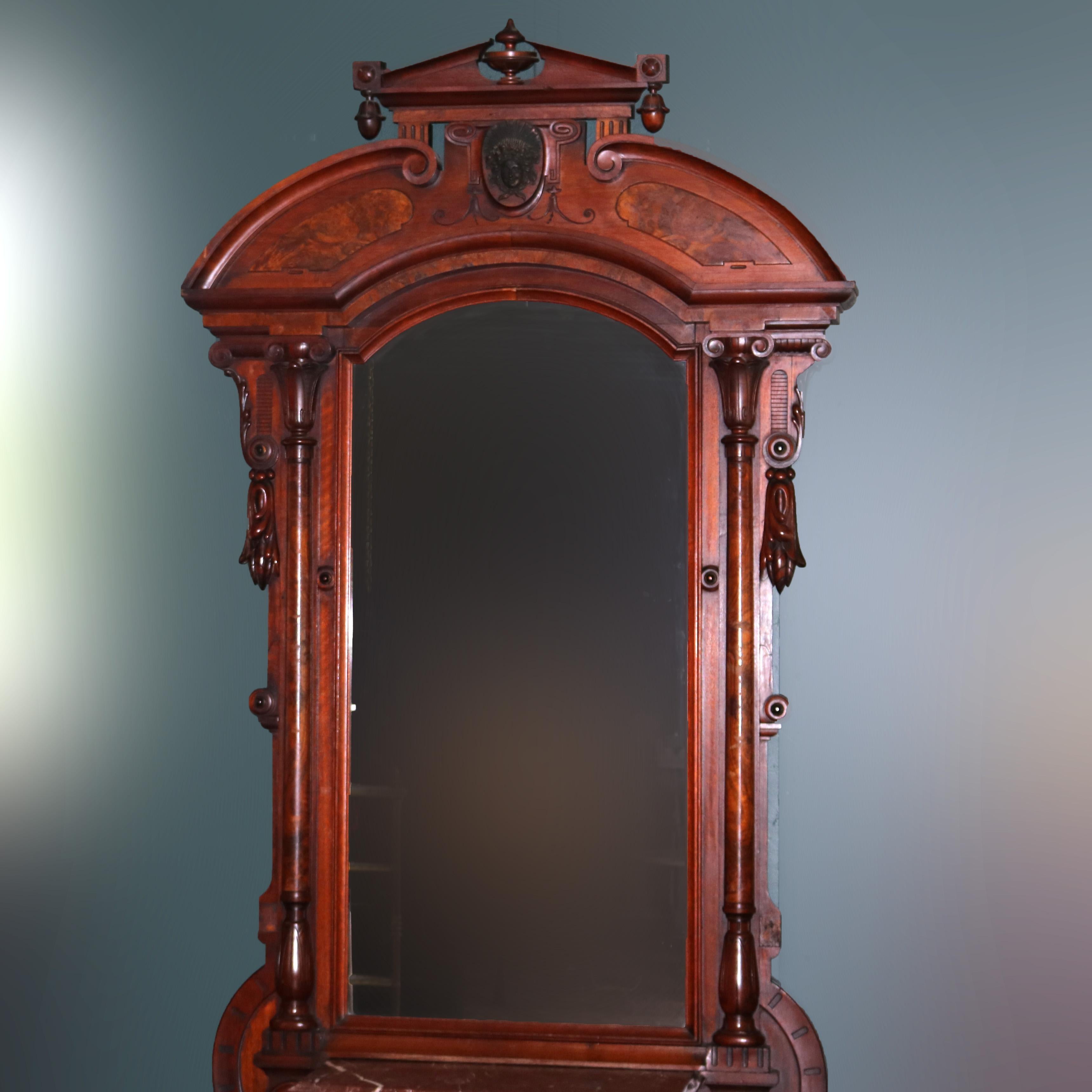 A monumental pier mirror by John Jelliff offers walnut and burl construction with broken arch crest having central urn, carved mask, and drop finials surmounting mirror with flanking columns, tassels, scroll and foliate elements over marble top base