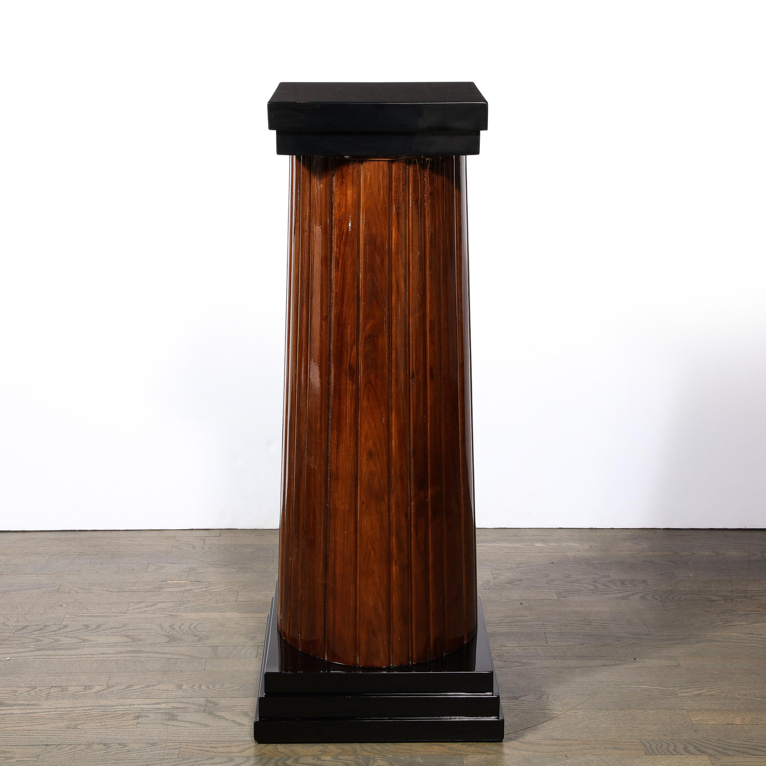This monumental and impressive Art Deco pedestal was realized in the United States circa 1940. It features a skyscraper style base consisting of three stacked tiers of lustrous black lacquer that supports a fluted column in walnut and is crowned by