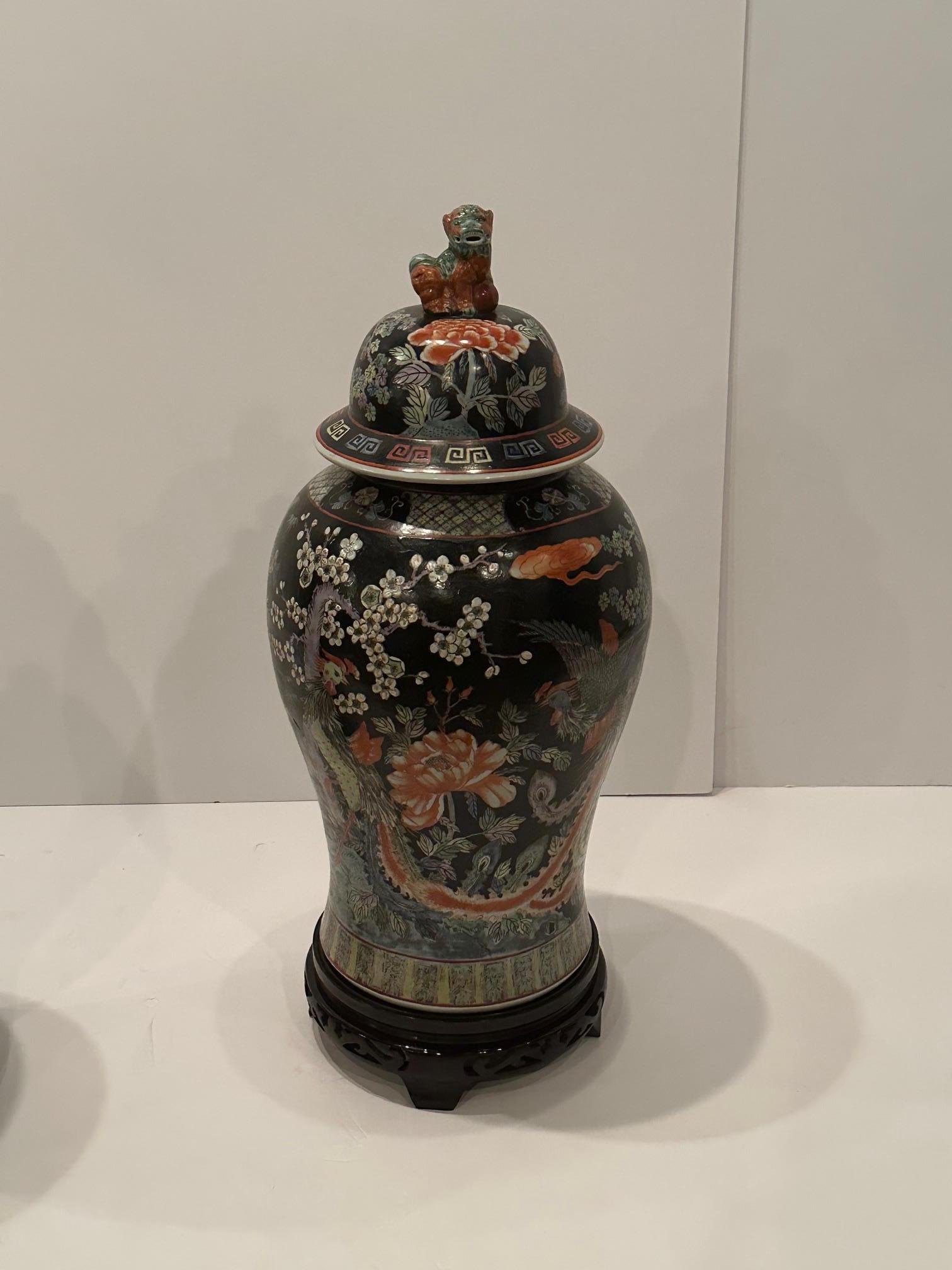 Impressively large intricately painted porcelain lidded urns having striking black background and decorated with cranes, birds, and other flowers.  Foo dog finials adorn the lids.
Lacquered ebonized wood stands are an elegant touch.