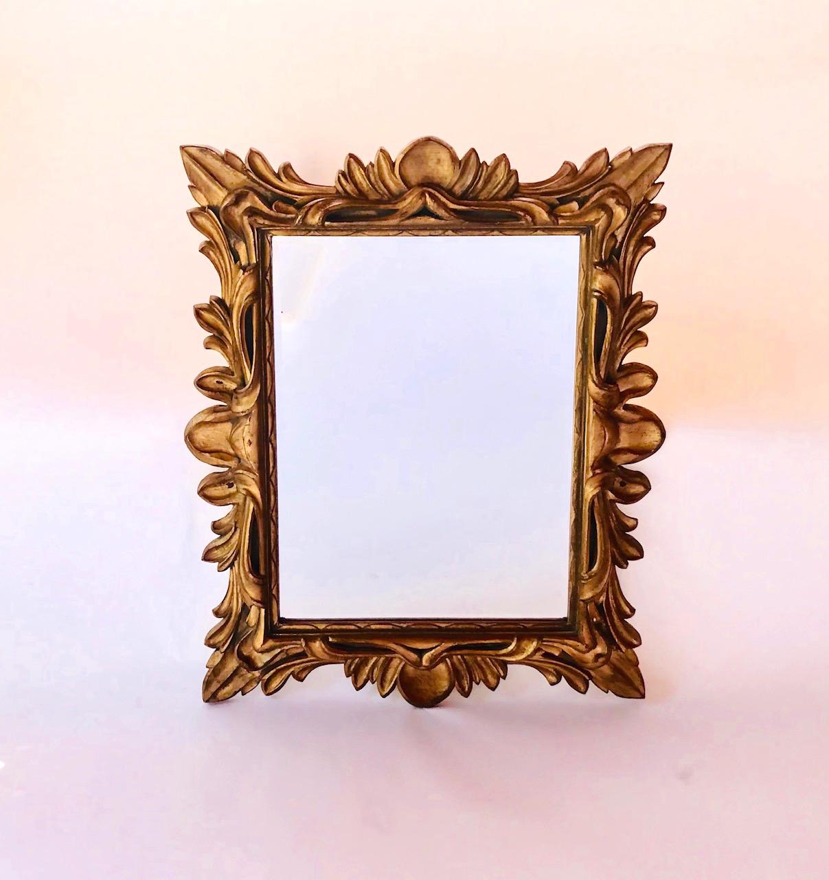 Hollywood Regency Baroque style large-scale mirror with spectacular ornate leaf frame. Antiqued gold leaf finish over molded resin frame with scrolled designs. Inner frame features scalloped carved wood and large hand-bevelled glass mirror.