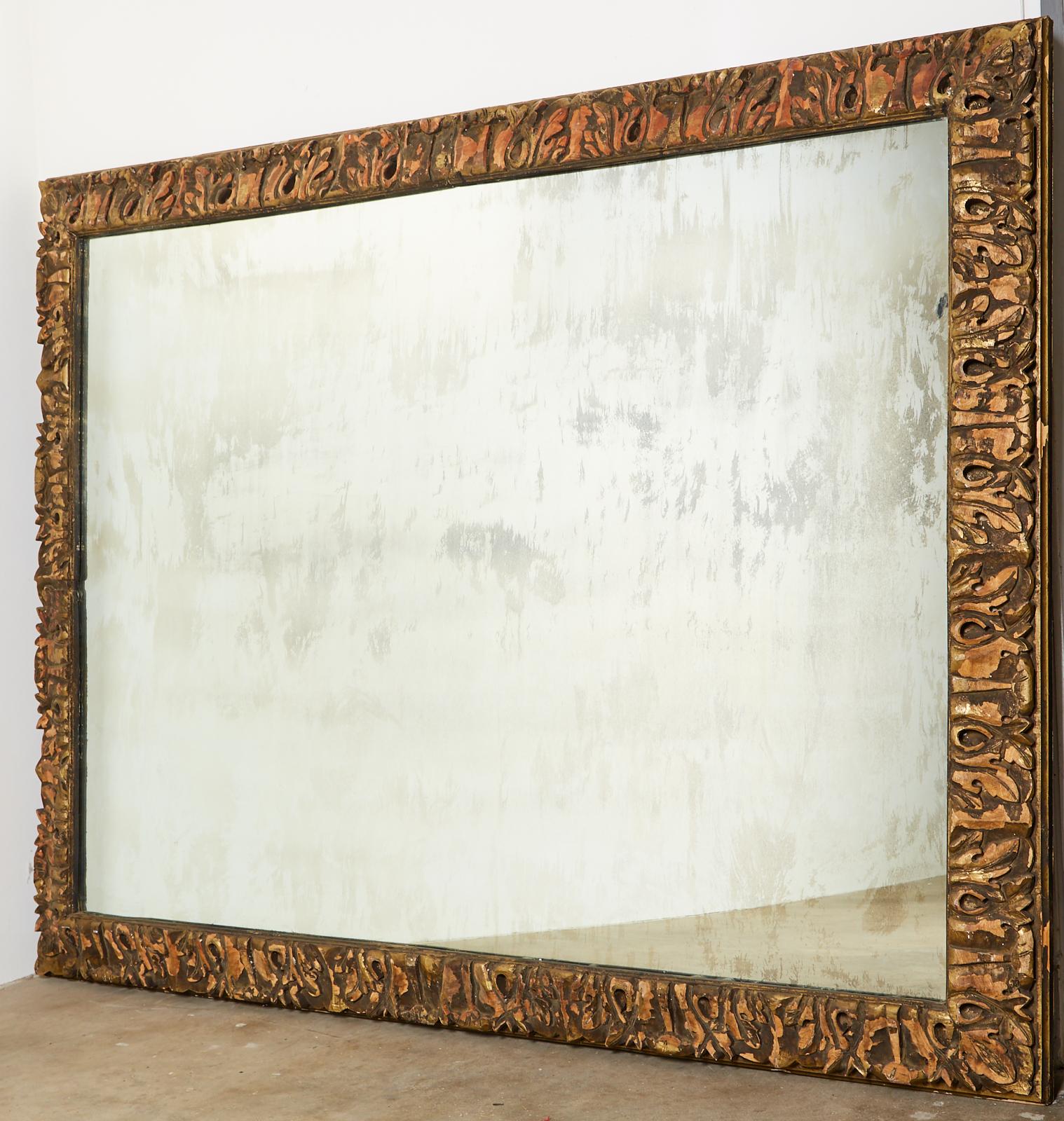Monumental custom made mirror featuring a thick, hand-carved parcel gilt frame. The mirror is decorated with stylized acanthus leaves having an aged and distressed patina. The large glass has intentional wear and age also. Bespoke mirror made for a