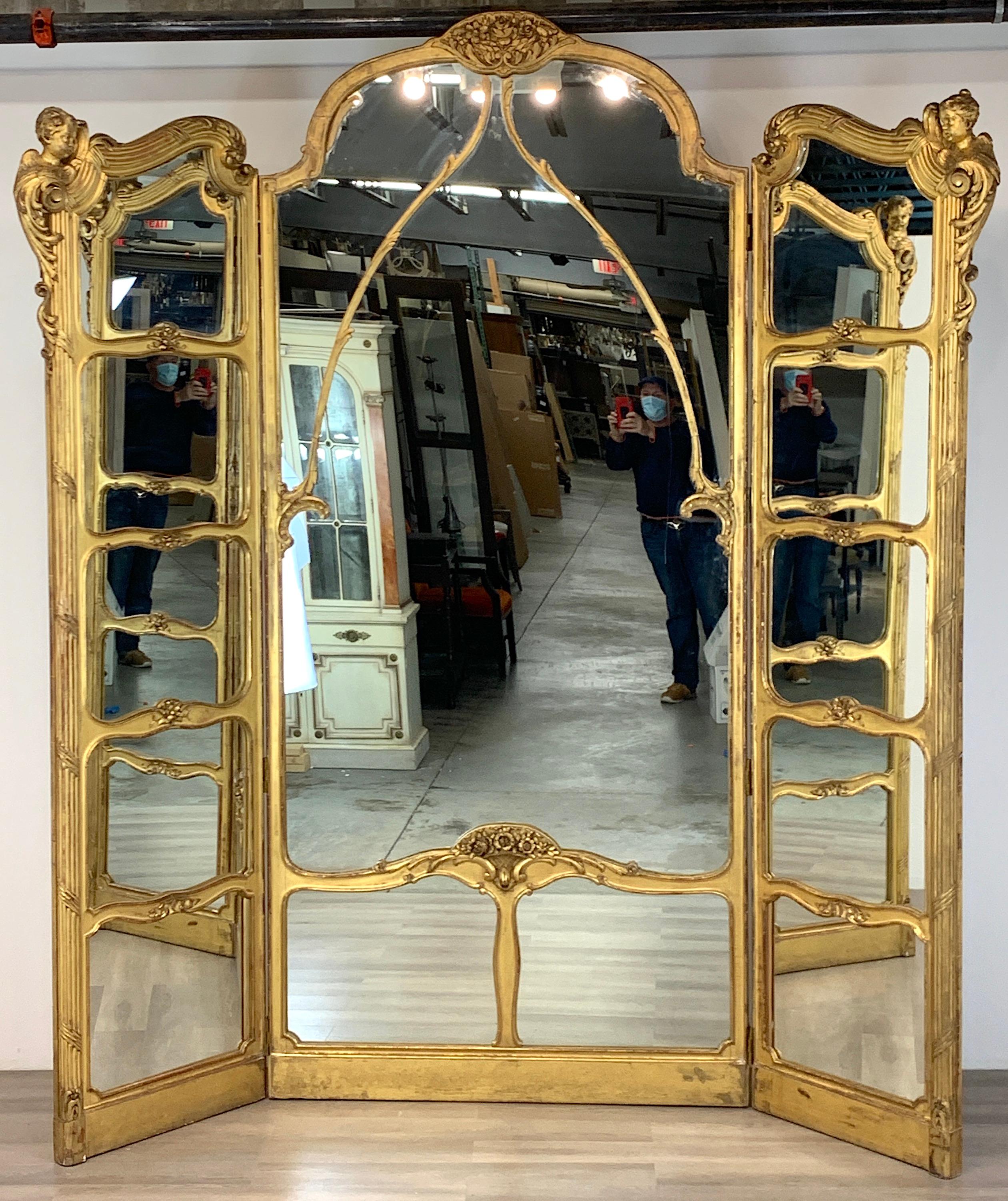 Monumental Belle Époque carved giltwood dressing mirror, Paris, circa 1880, subtle and sublime three-panel giltwood mirror screen. The center panel measures 9 feet high x 4 feet wide. The two flanking carved cherub panels measure 8 feet high x 2