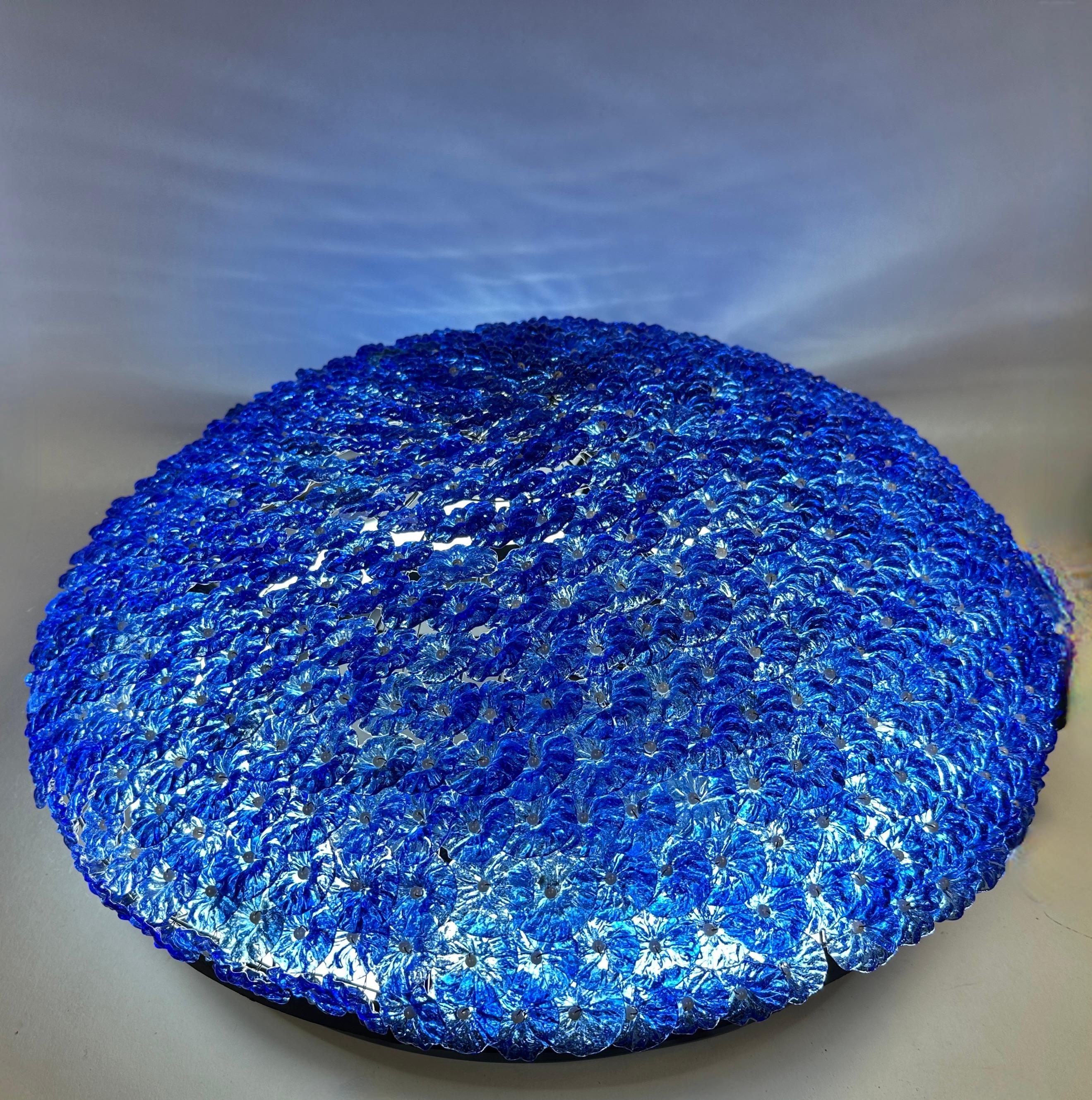 The chandelier is made of blue Murano glass flowers, over a round metal gridded frame. The Fixture requires four European E14 / 110 Volt Candelabra bulbs, each bulb up to 60 watts. It is translucent and gives off a beautiful warm bluish light when