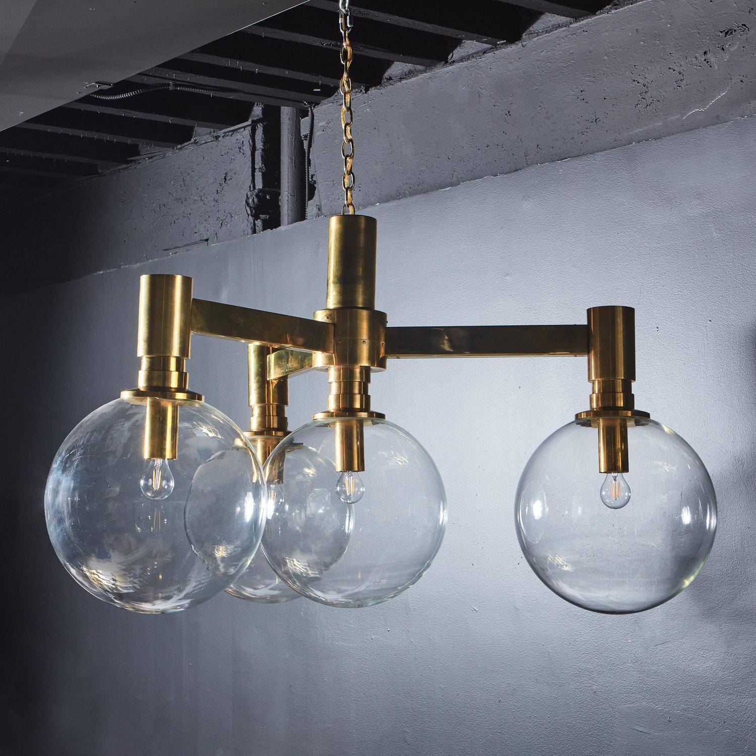 A beautiful vintage 1960s Austrian chandelier featuring an elegant polished brass frame with three angular arms. This fixture has four oversized hand blown spherical shades, creating a dramatic contrast to the monumental frame. 

Fixture Measures