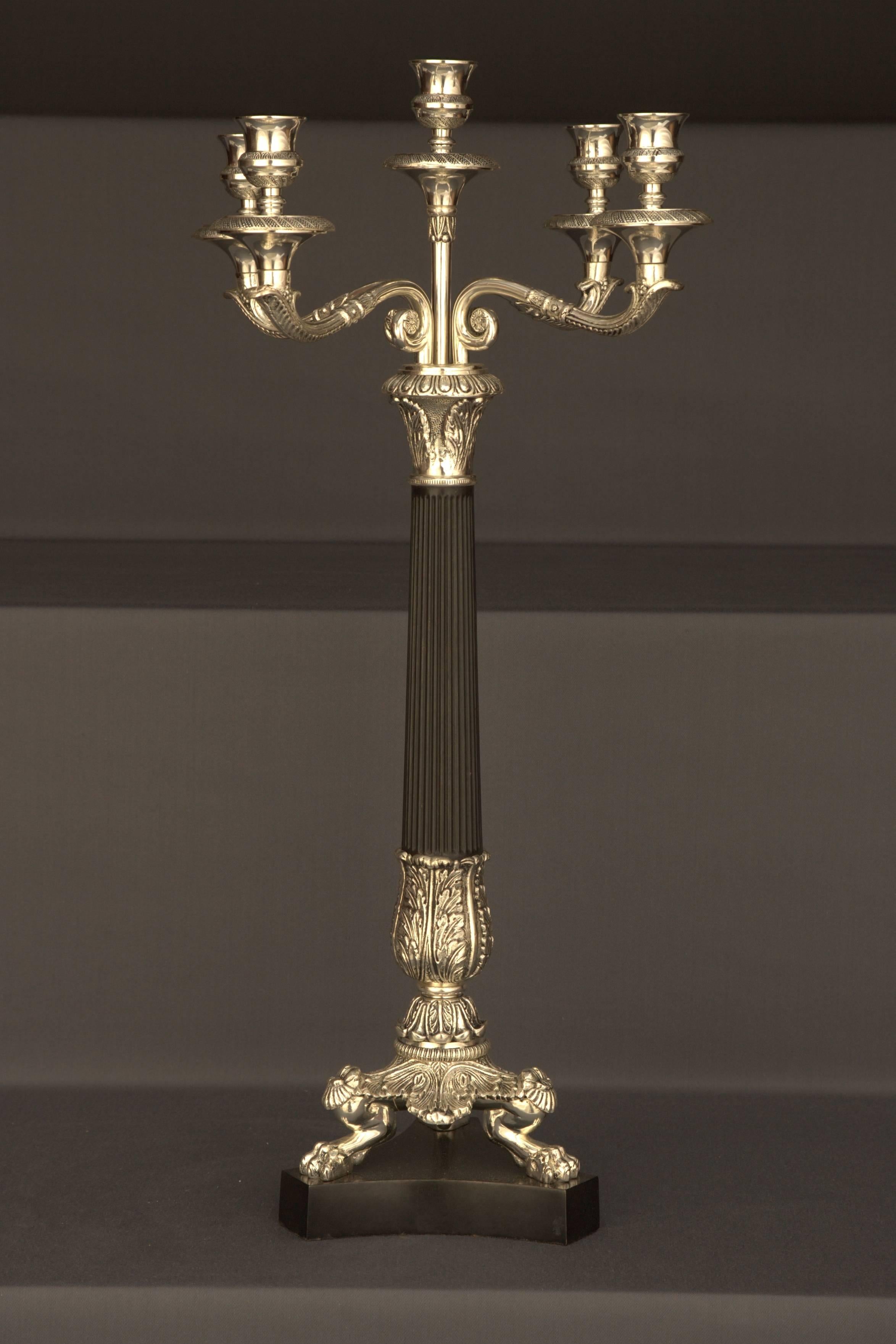 Bronzo, finemente inciso e argentato. Colonne con decorazioni a forma di gallone con
patinatura nera, come supporto per quattro bracci di candelabro.
Misure: 
Diametro 33 cm, 
altezza 62 cm.
