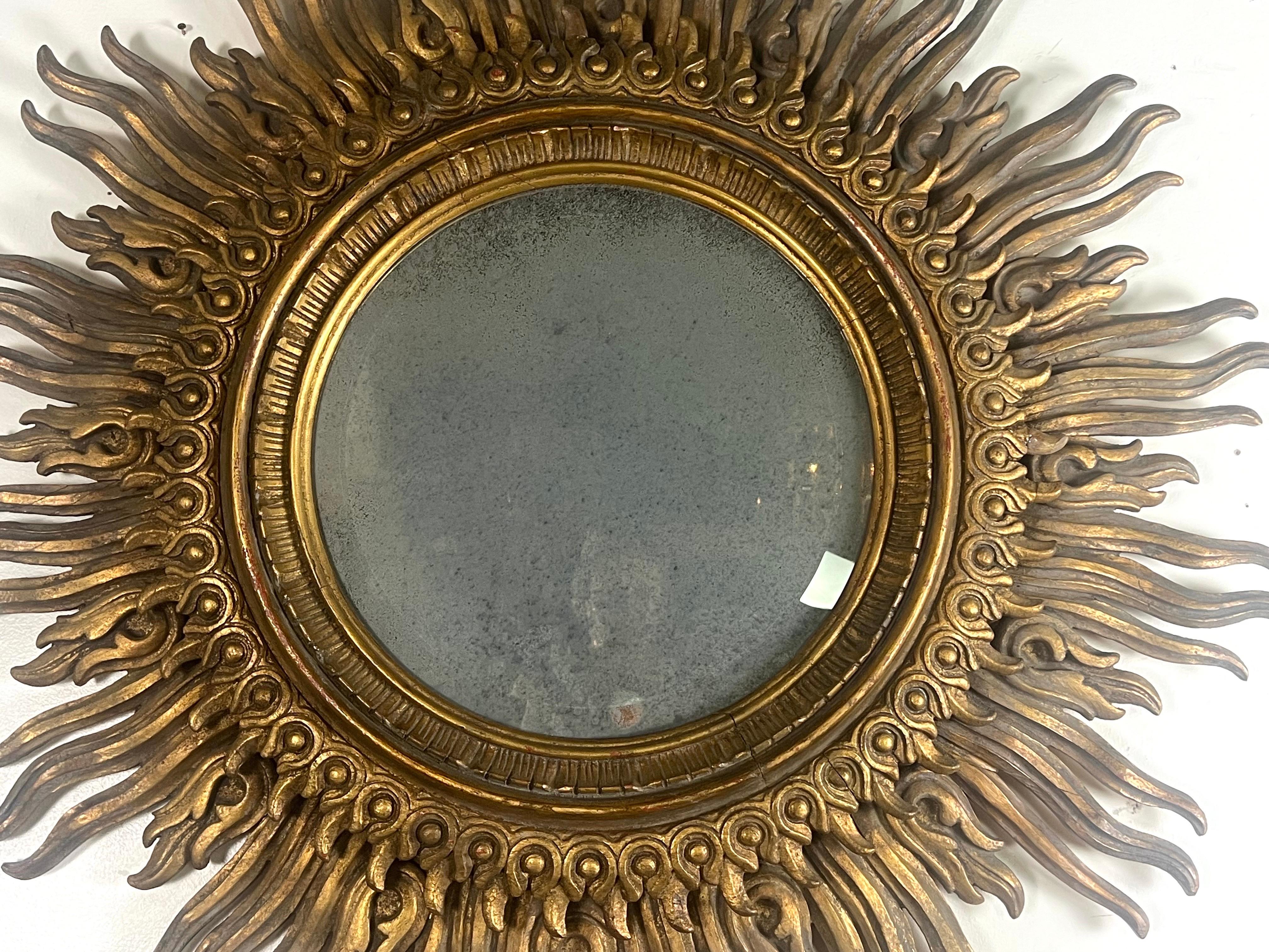 This Italian giltwood sunburst mirror, monumental in scale, is an exquisite piece that captures the lavishness and artistry of Italian craftsmanship.  The mirror features a central glass panel that is beautifully antiqued, giving it a vintage charm