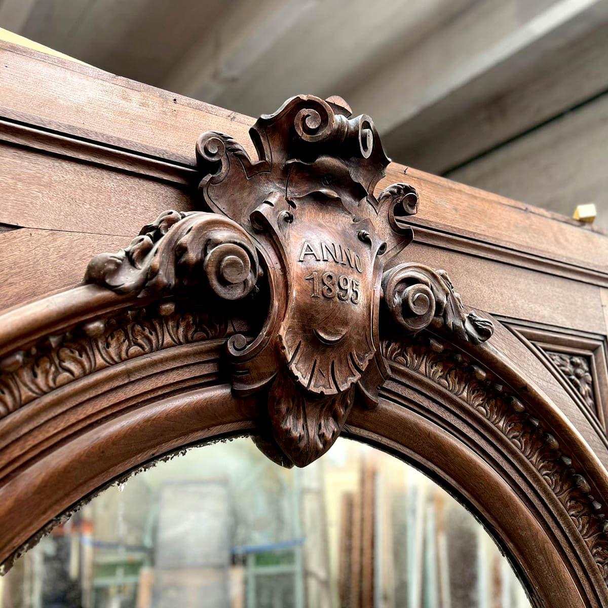 Impressive and richly detailed trumeau mirror carved from solid oak, dated Anno 1895. This architectural piece features a striking arched mirror set within a robust oak frame adorned with hand-carved floral and scrollwork motifs. The central crest