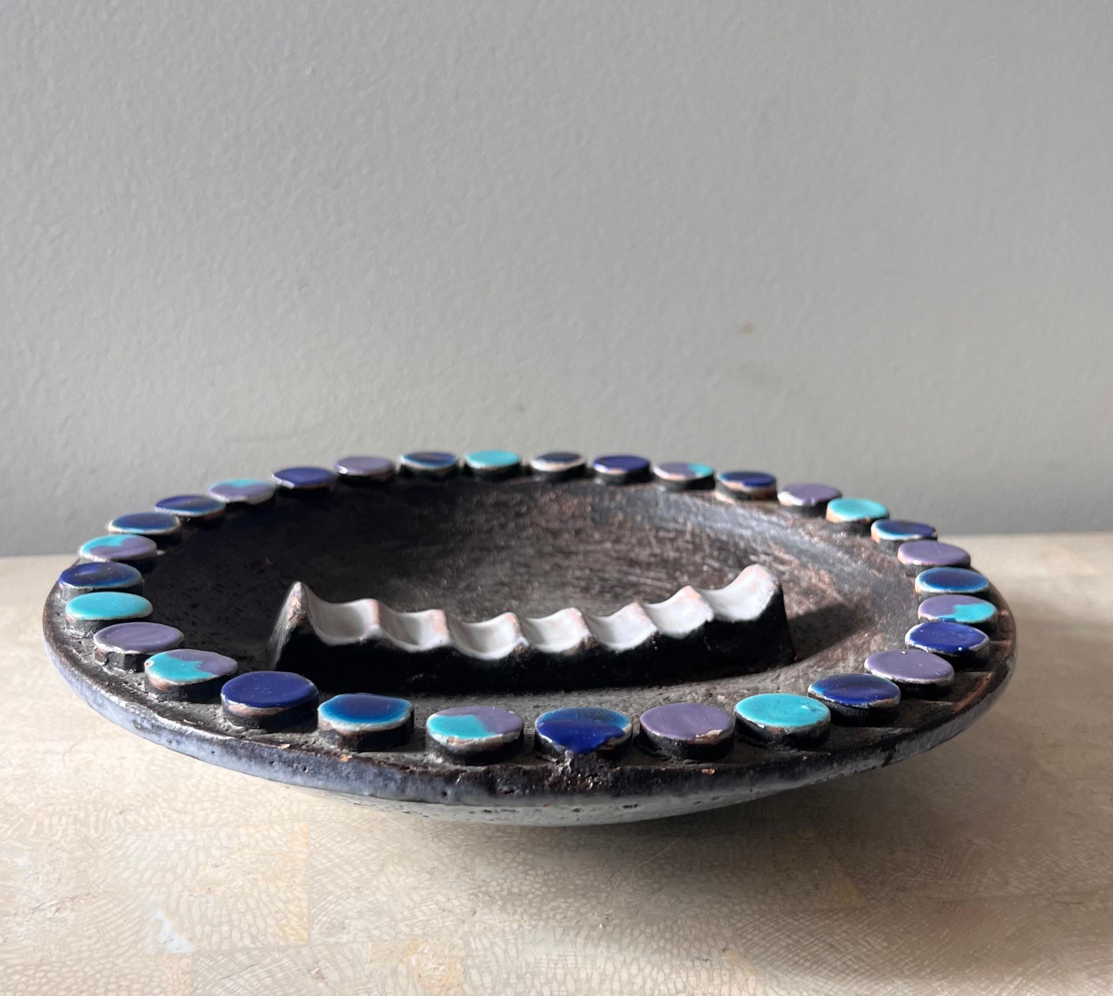 A monumental mid century modern ceramic ashtray by Aldo Londi for Bitossi, Italy circa 1960s. Tones of pewter, turquoise, lavender, and Yves Klein blue, and featuring 7 rivulets in center. Some wear to the colored tiles adorning the edge, but