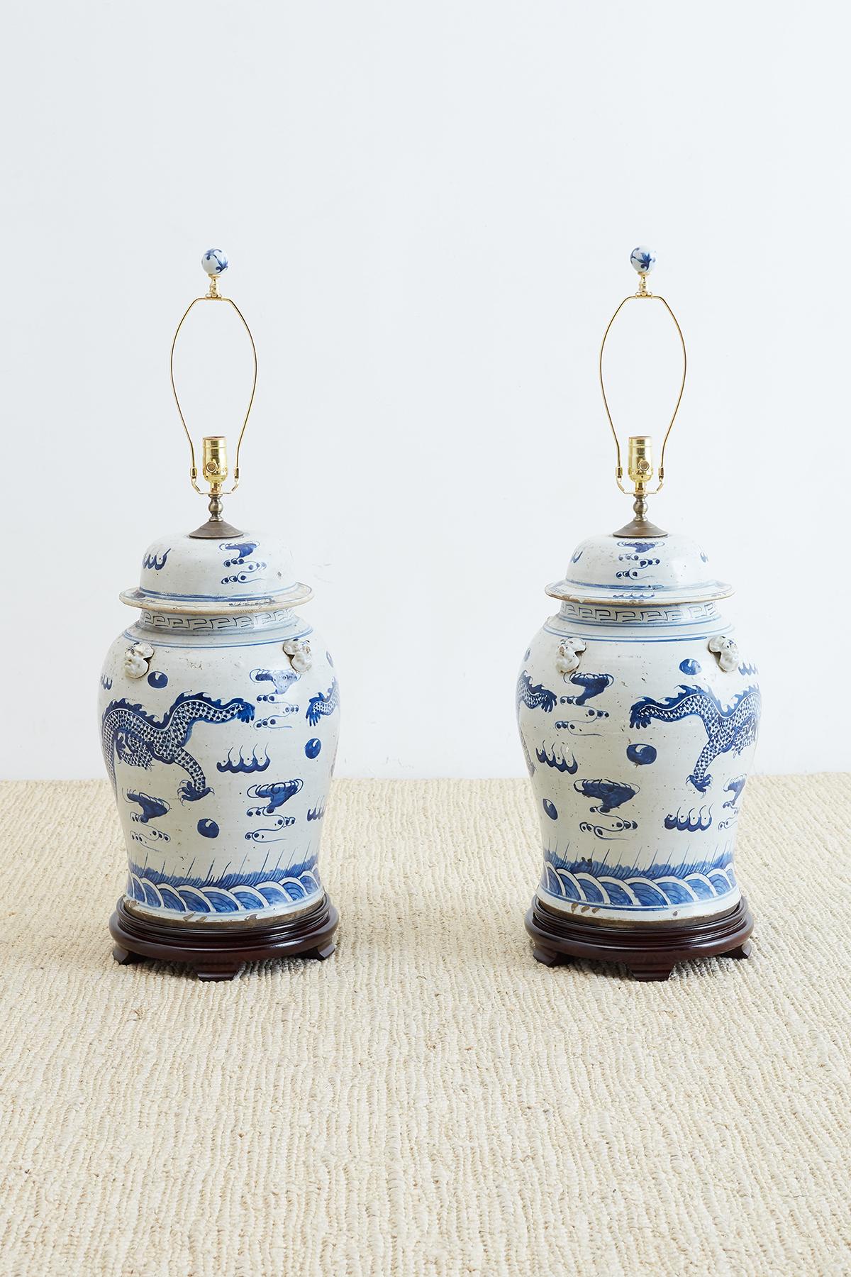 Fantastic pair of monumental Chinese blue and white ginger jars converted to table lamps. Hand-painted with dragons in the clouds over a sea of waves. Mythical beast heads adorn the shoulders on each side. Mounted to wooden plinths with shaped feet.