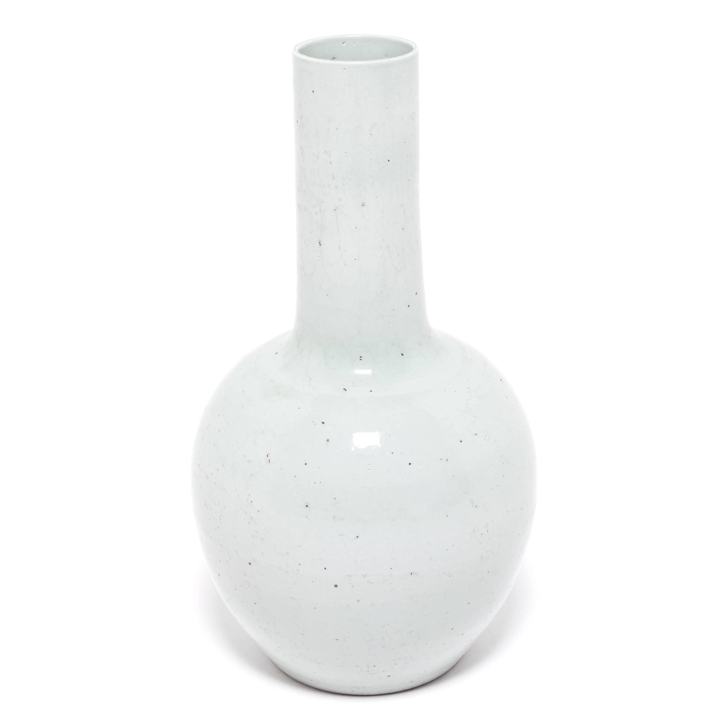Drawing on a long Chinese tradition of monochrome ceramics, this tall gooseneck vase is glazed in serene pale celadon. The vase features a rounded, globular body and a narrow cylindrical neck, a classic form known as 'tianqiuping' or 'celestial ball