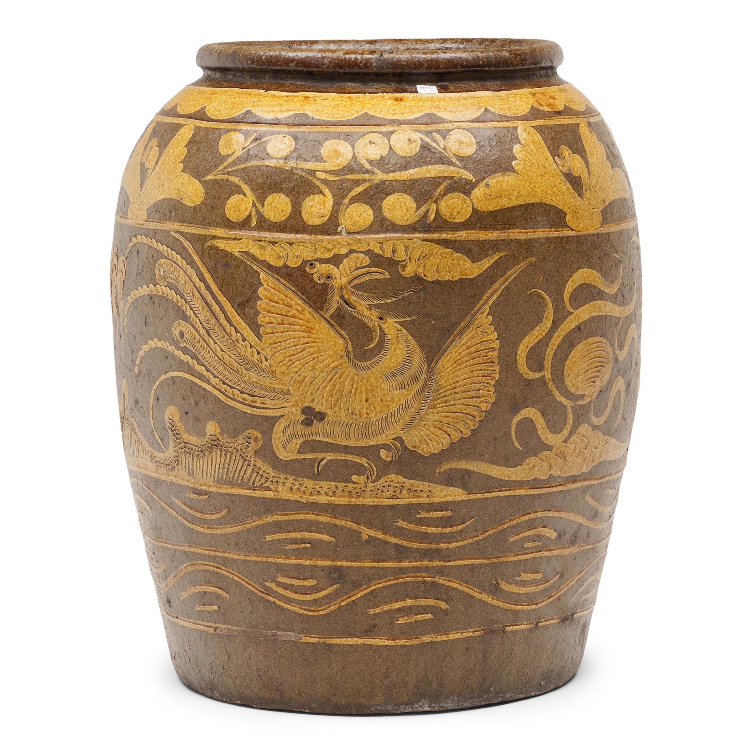 This monumental ceramic vessel is a 19th century Chinese pickling jar, decorated in shallow relief with a brown and mustard-yellow glazed finish. Large glazed earthenware jars such as this were used for storing dry food, pickling vegetables or