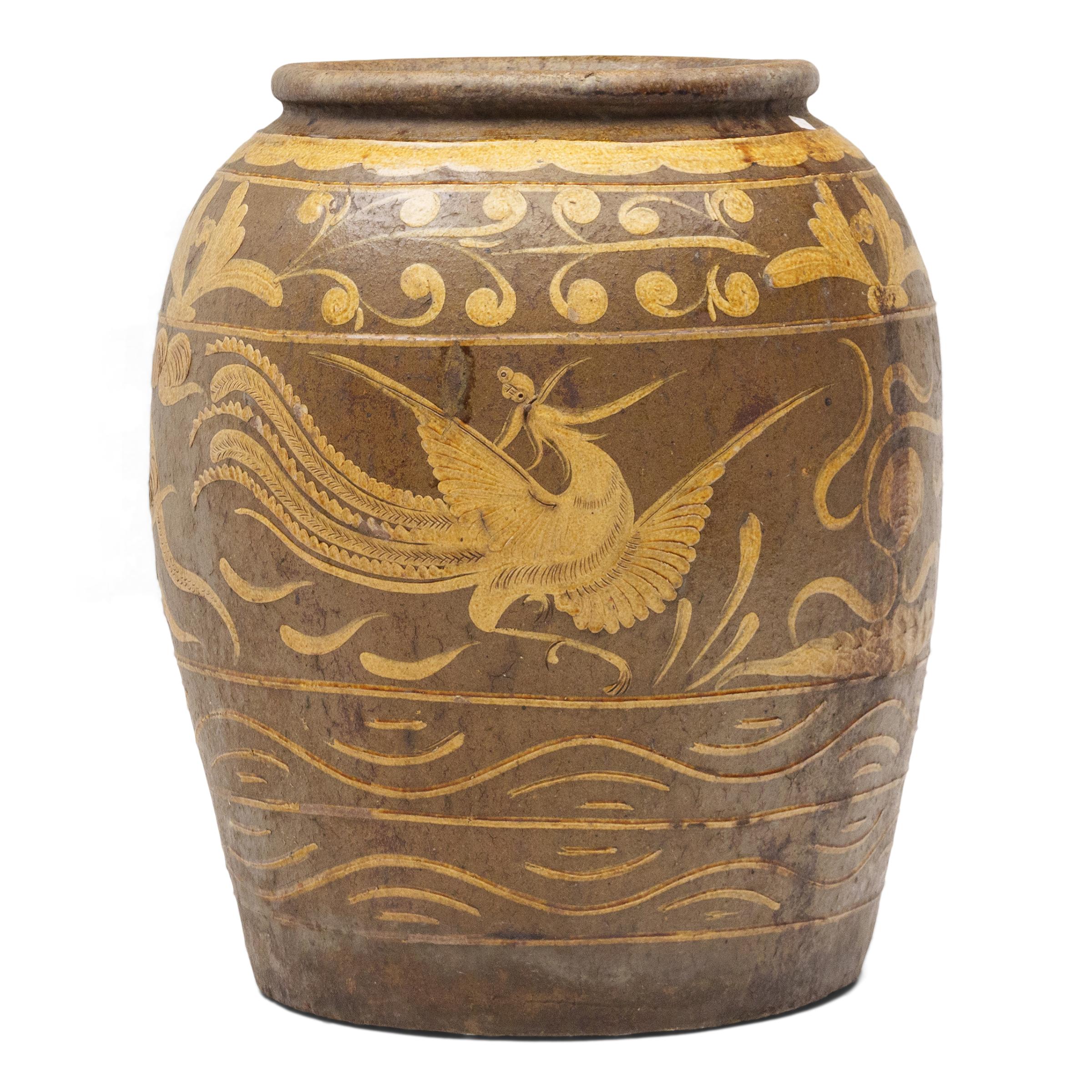 This monumental ceramic vessel is a 19th century Chinese pickling jar, decorated in shallow relief with a brown and mustard-yellow glazed finish. Large glazed earthenware jars such as this were used for storing dry food, pickling vegetables or