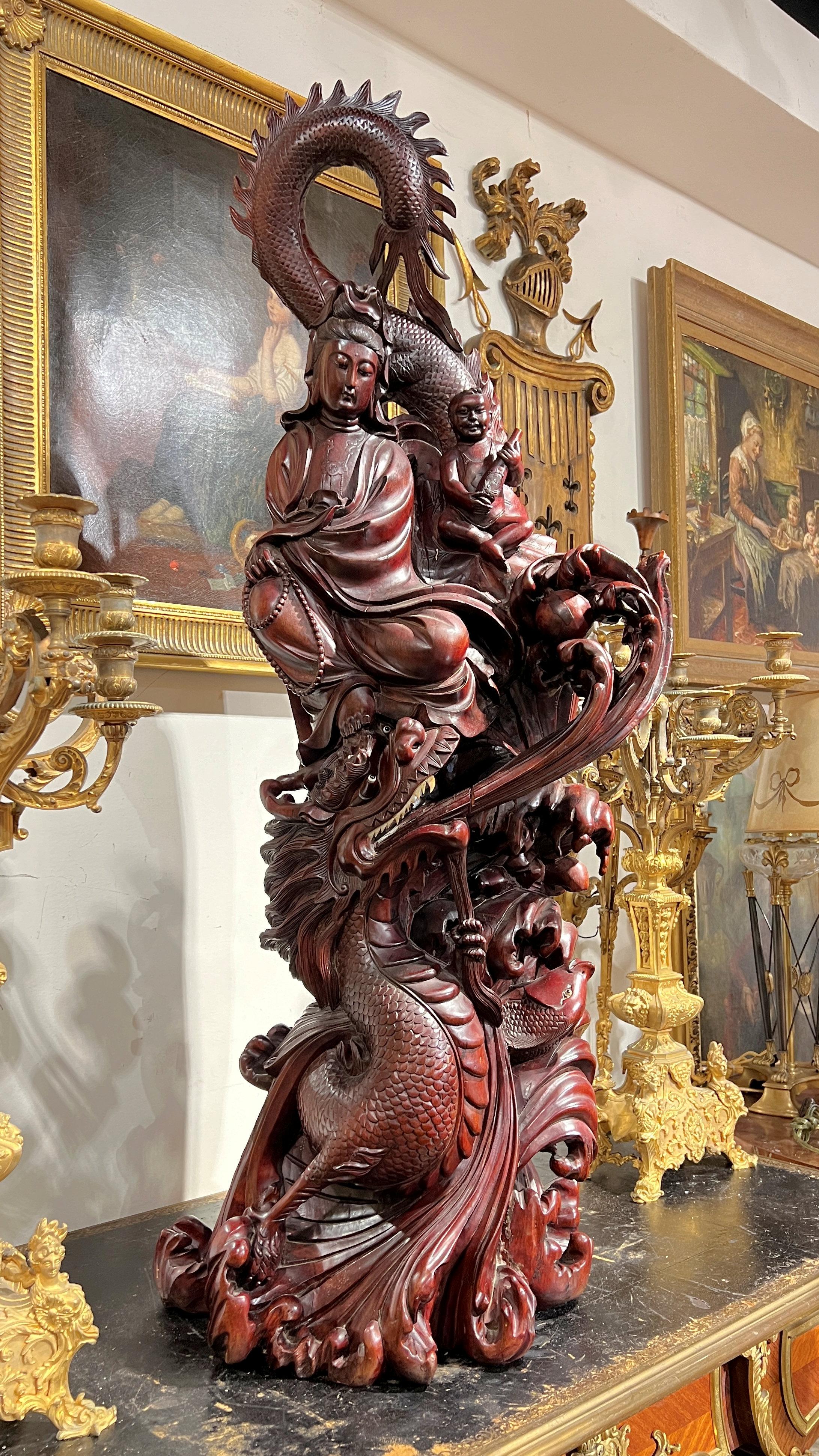 Monumental, vintage sculpture in carved rosewood of Quan Yin (Guanyin) measuring 50.5 by by 22 by 14 inches, depicting the Buddhist goddess of mercy and compassion, draped with a fierce dragon, the symbolic of wisdom, strength and wisdom, with a