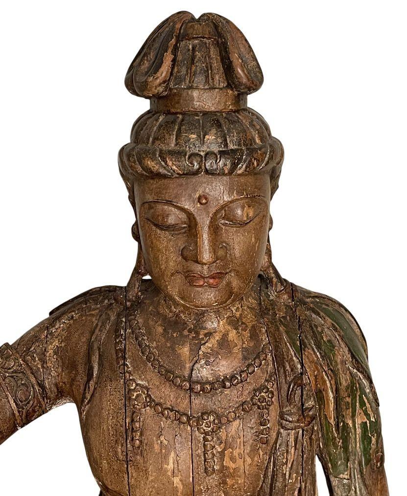 Un'imponente e serena scultura in legno intagliato di Guanyin, il Bodhisattva della Compassione, realizzata nello stile della dinastia Song. Questa figura monumentale è graziosamente posata in 