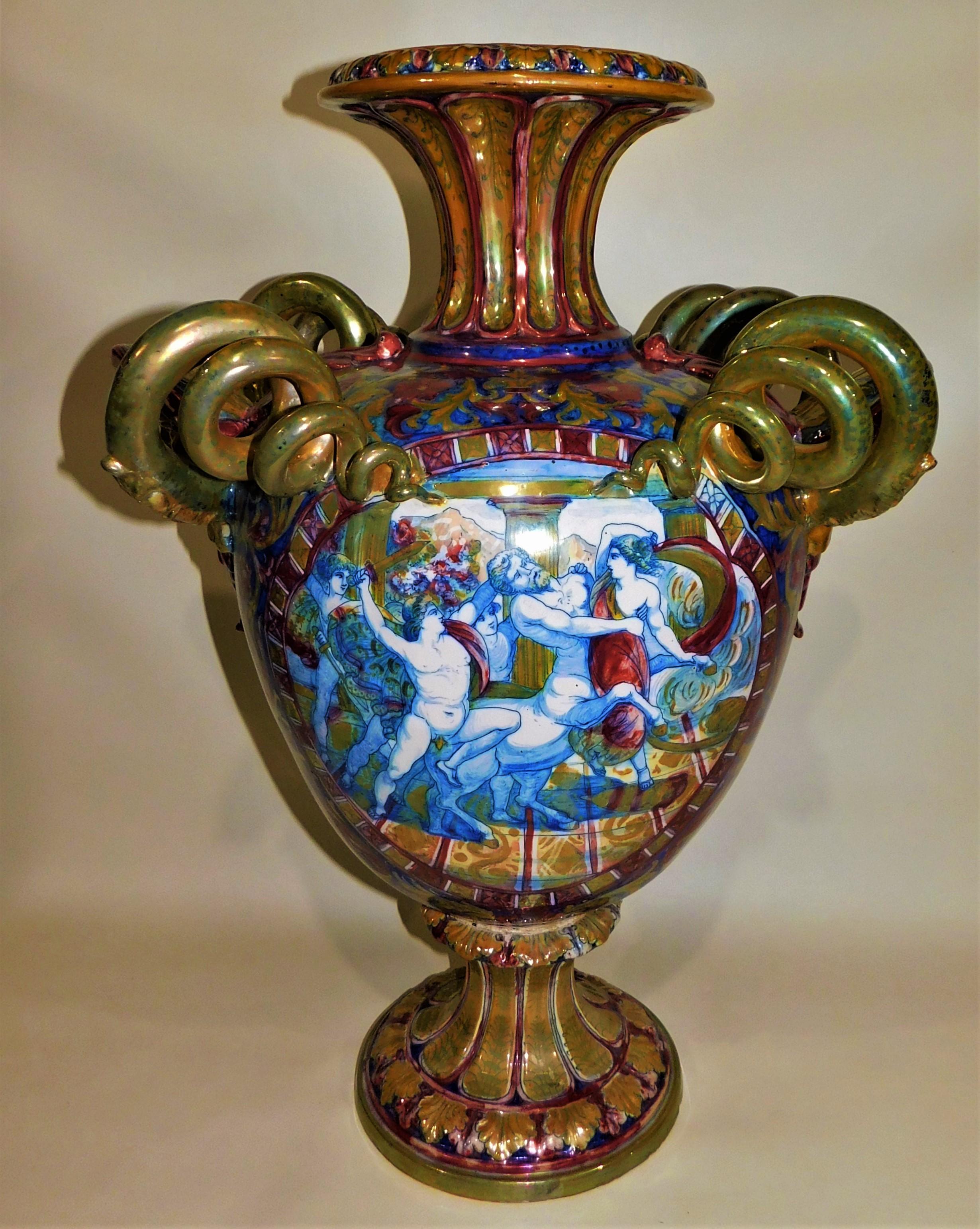 From Italy, this imposing antique hand painted Majolica luster glazed ceramic pottery urn shaped vase with serpent like handles is over two feet high. It is mainly a figural vase in style, having beautiful hand painted with allegorical scenes within