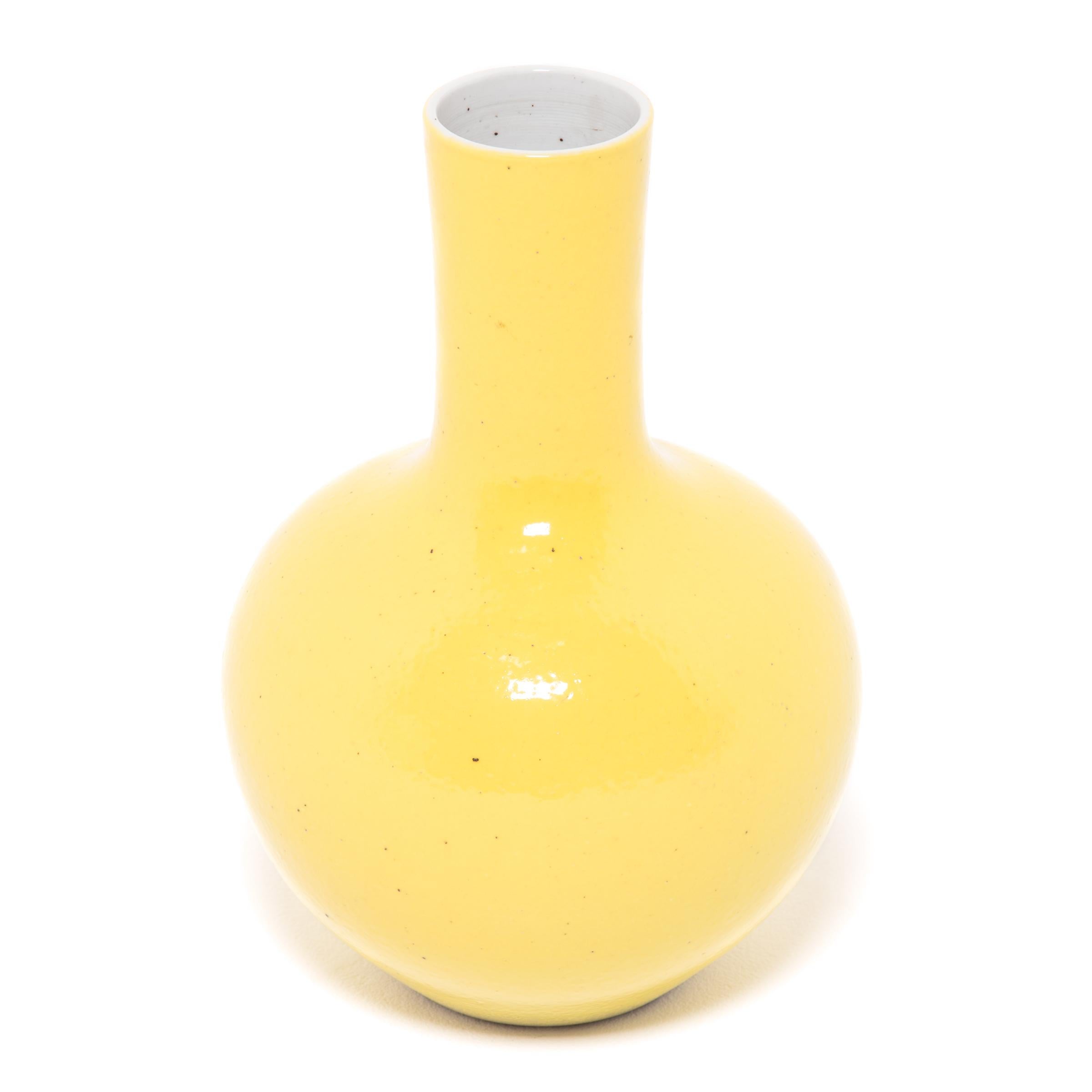 Drawing on a long Chinese tradition of monochrome ceramics, this tall gooseneck vase is glazed in cheerful citron-yellow glaze. The vase features a rounded, globular body and a narrow cylindrical neck, a classic form known as 'tianqiuping' or