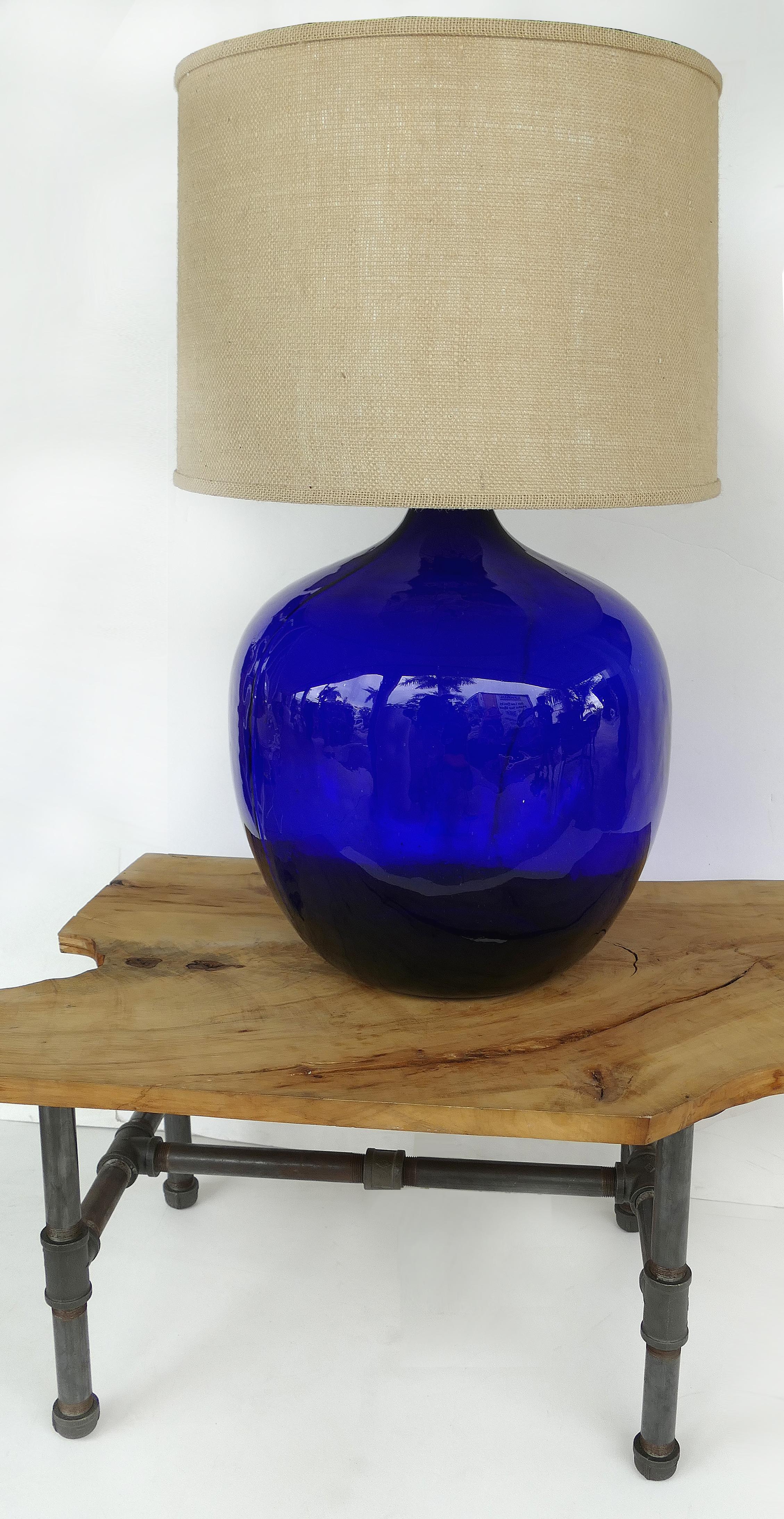 Monumental cobalt blue blown glass table lamp with burlap shade


Offered for sale is an over-scale vintage cobalt blue glass table lamp fitted with a burlap drum shade. The cobalt glass is hand blown in the style of Blenko glass and the coloring
