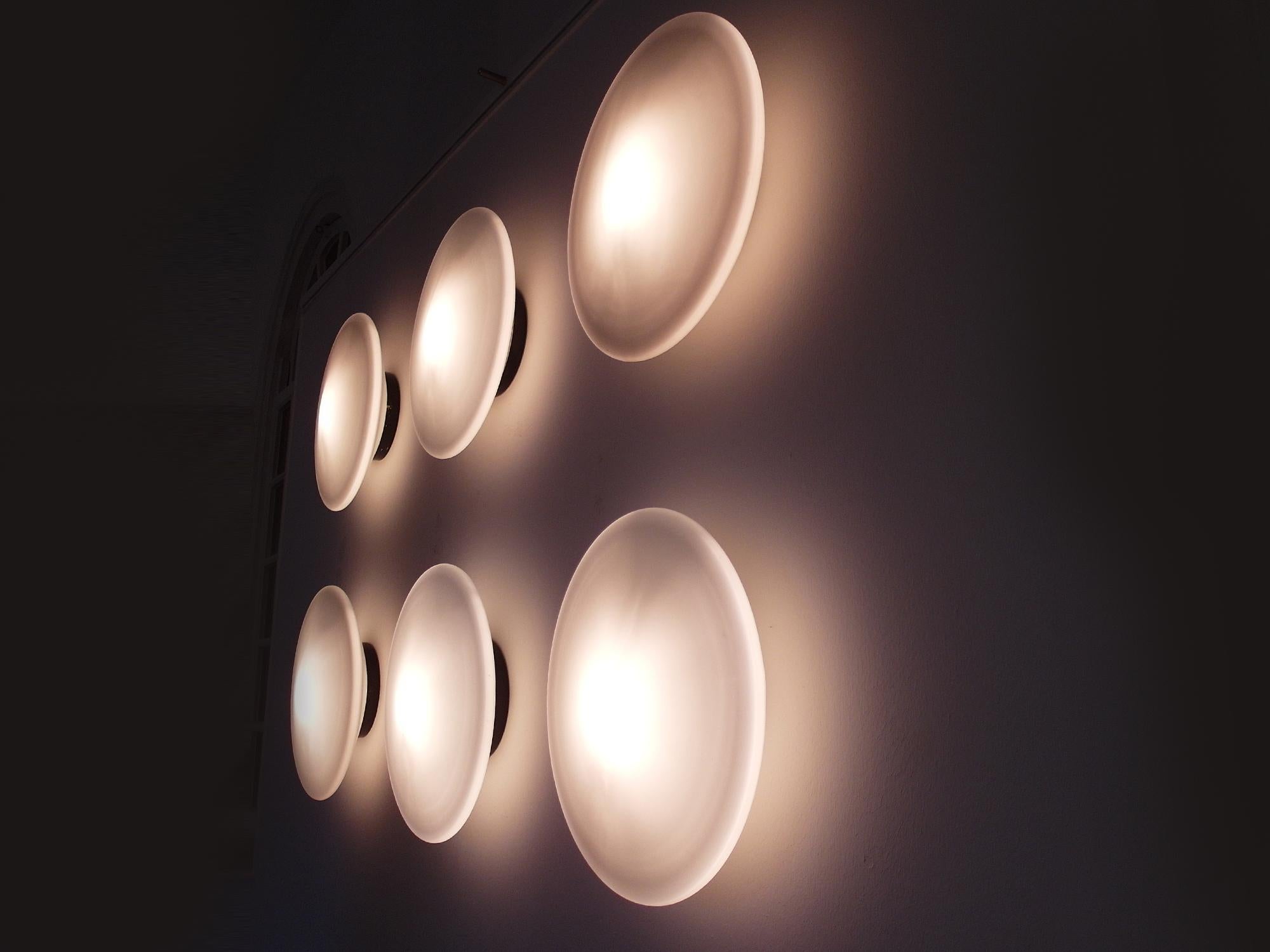Monumental set of six largest version RAAK B-1412 opaline glass RAAK Discus lights designed by RAAK Amsterdam, The Netherlands 1952. Composed as an installation on the wall, these six Minimalist Discus sconces made of black metal and original
