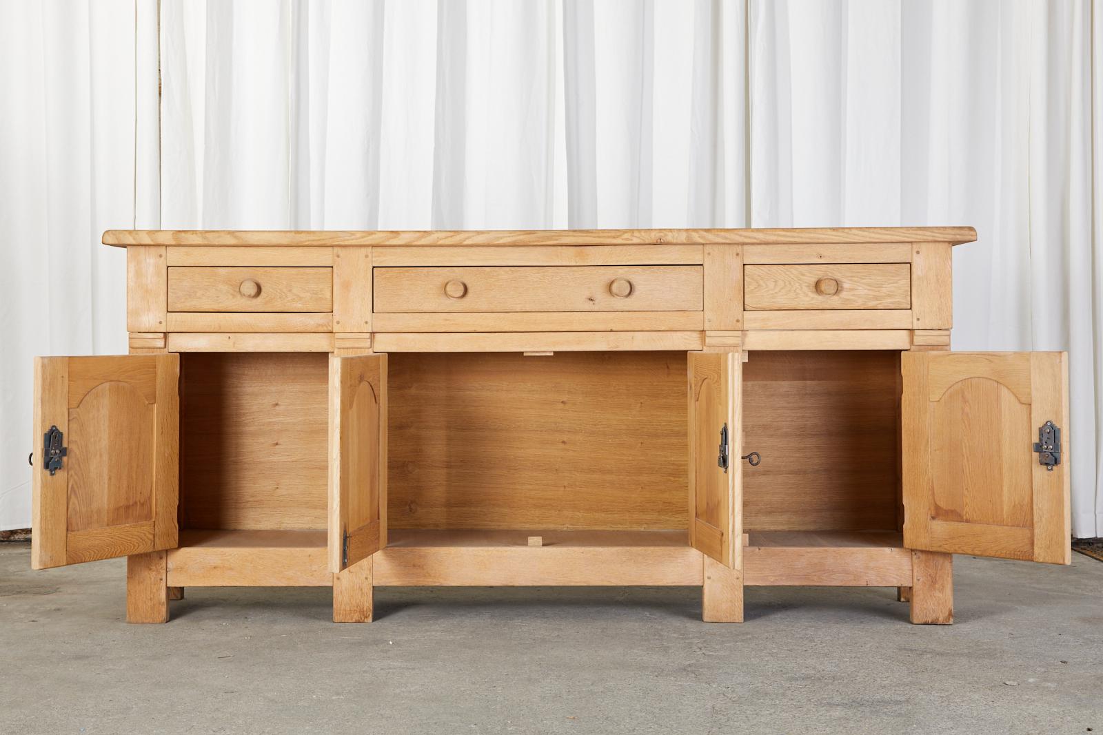 Monumental two-part sideboard server, buffet, or dresser made in the country French taste. The case features a bleached oak finish with a lovely aged and faded patina. The top part has three storage drawers with round wood pulls. The bottom case is