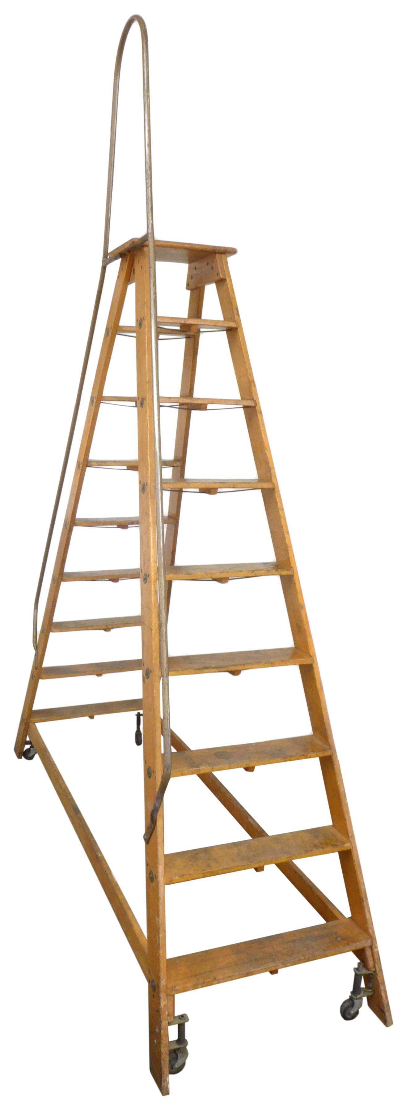 A monumental, double sided wood ladder. Towering at over 10' high, a simple and Classic utilitarian form in an impressive and unusual scale. Spring-loaded casters at the base make for easy movement. A tubular steel hand-rail accompanies one side of