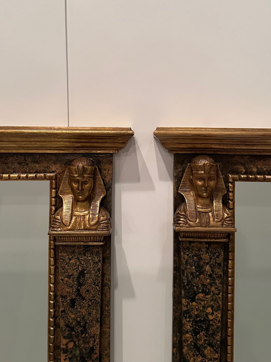 Coppia ornata e drammatica di specchi giganti in legno marmorizzato e dorato di epoca Revival egiziana con forme figurative su ciascun lato e dettagli di piedi sul fondo.