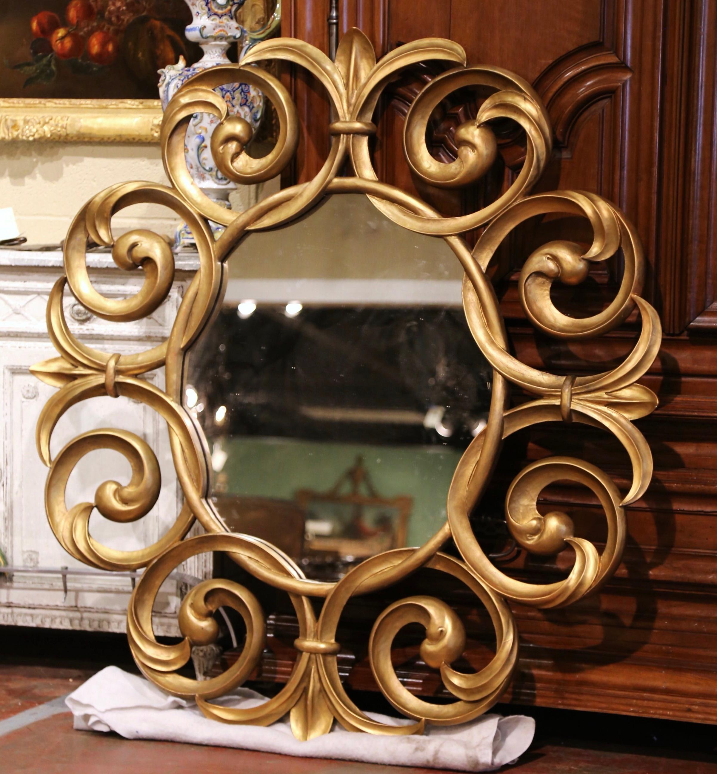 This important antique sunburst mirror was crafted in France, circa 1920. Almost 5 feet high and circular in shape, the large mirror features hand carved scroll and Fleur-de-Lys motifs in high relief throughout. The wall decor is dressed with a
