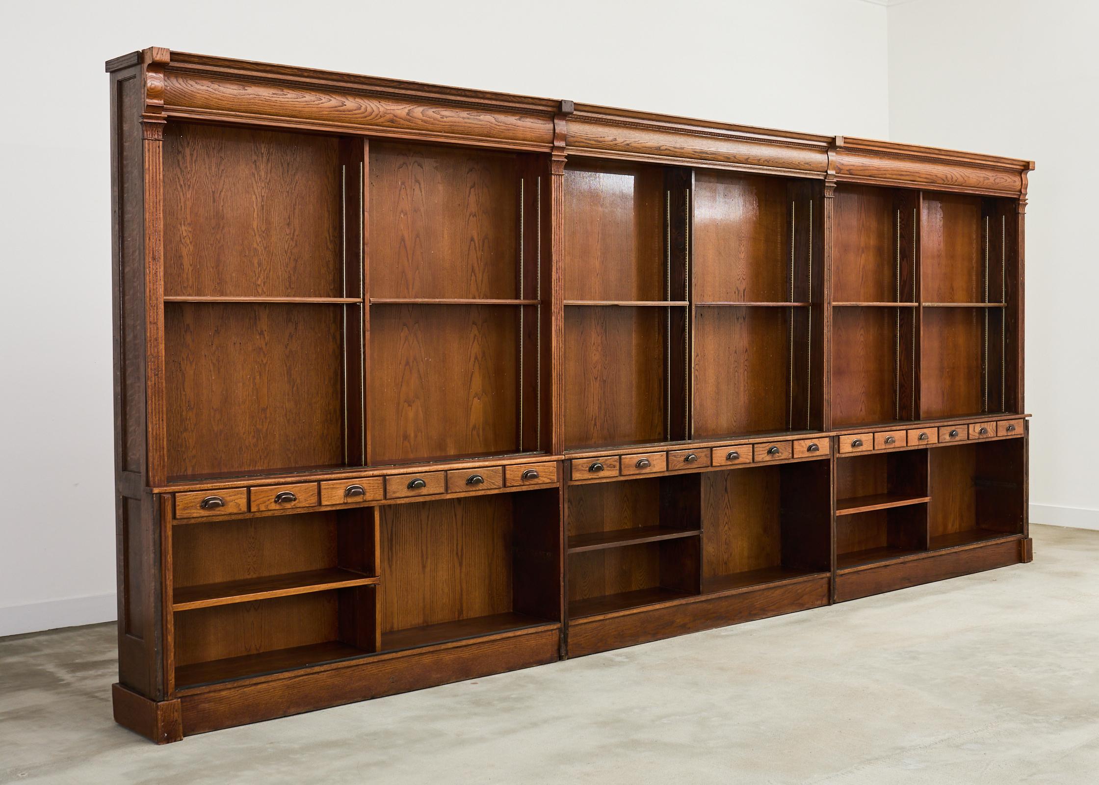 Grand English haberdashery store boutique display cabinet or bookcase crafted from oak on a monumental scale. The case measures over 18 feet wide with upper and lower open-shelved storage areas. The top of the cases feature a cornice molding with