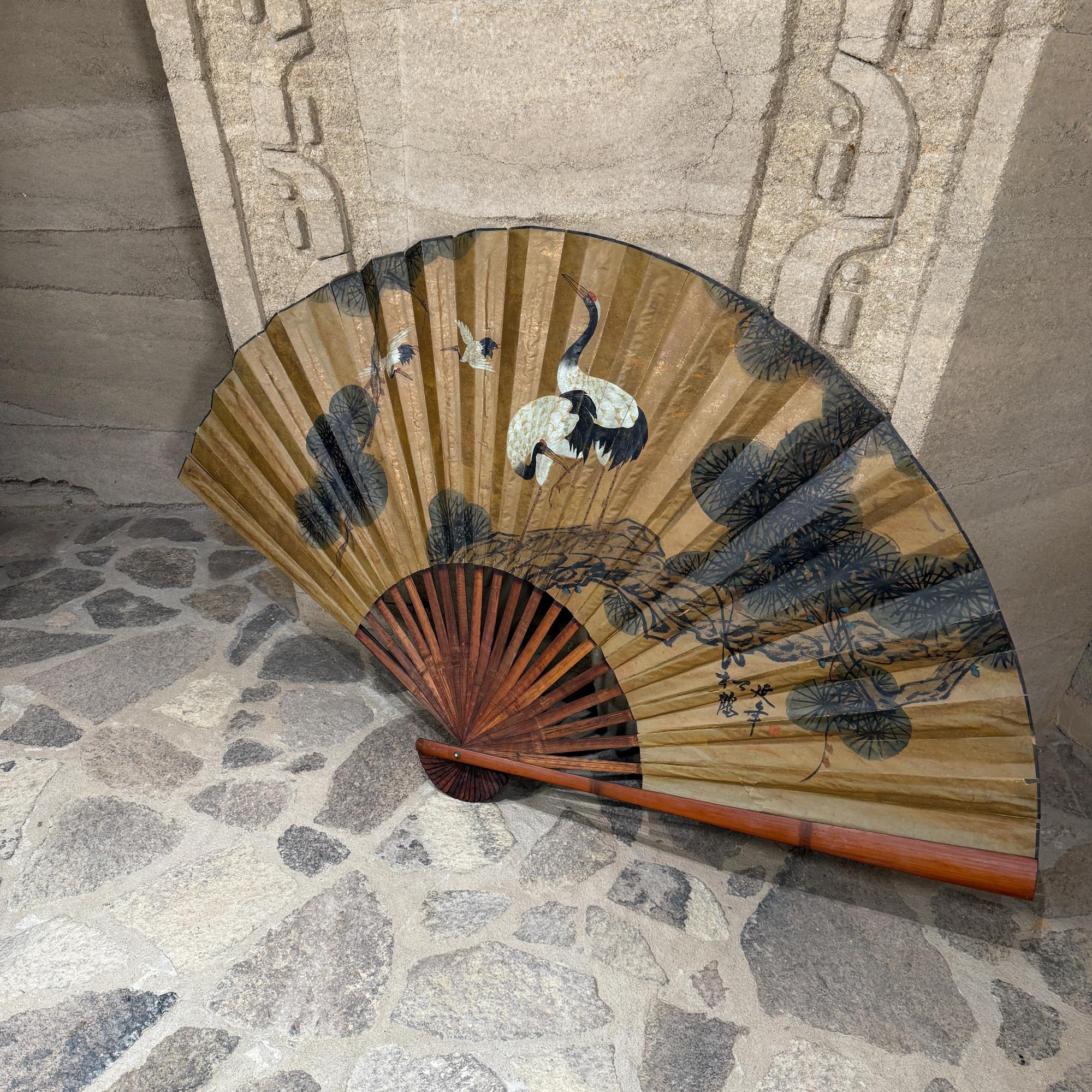 Zu sehen ist ein großer chinesischer Wandventilator im Vintage-Stil, der typischerweise für dekorative Zwecke verwendet wird. Diese handbemalten Fächer weisen häufig traditionelle Motive auf, wobei dieses Exemplar Kraniche und Kiefern zeigt.  Der