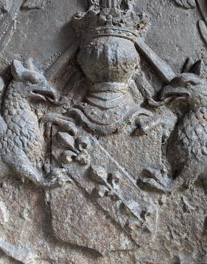 Cette exceptionnelle plaque de cheminée en fonte de 750 kg, richement décorée, a été réalisée à la fin de la Renaissance, vers 1624. Il porte en son centre un écu avec une bande chargée de trois fleurs de lys en argent, soutenue par deux griffons.