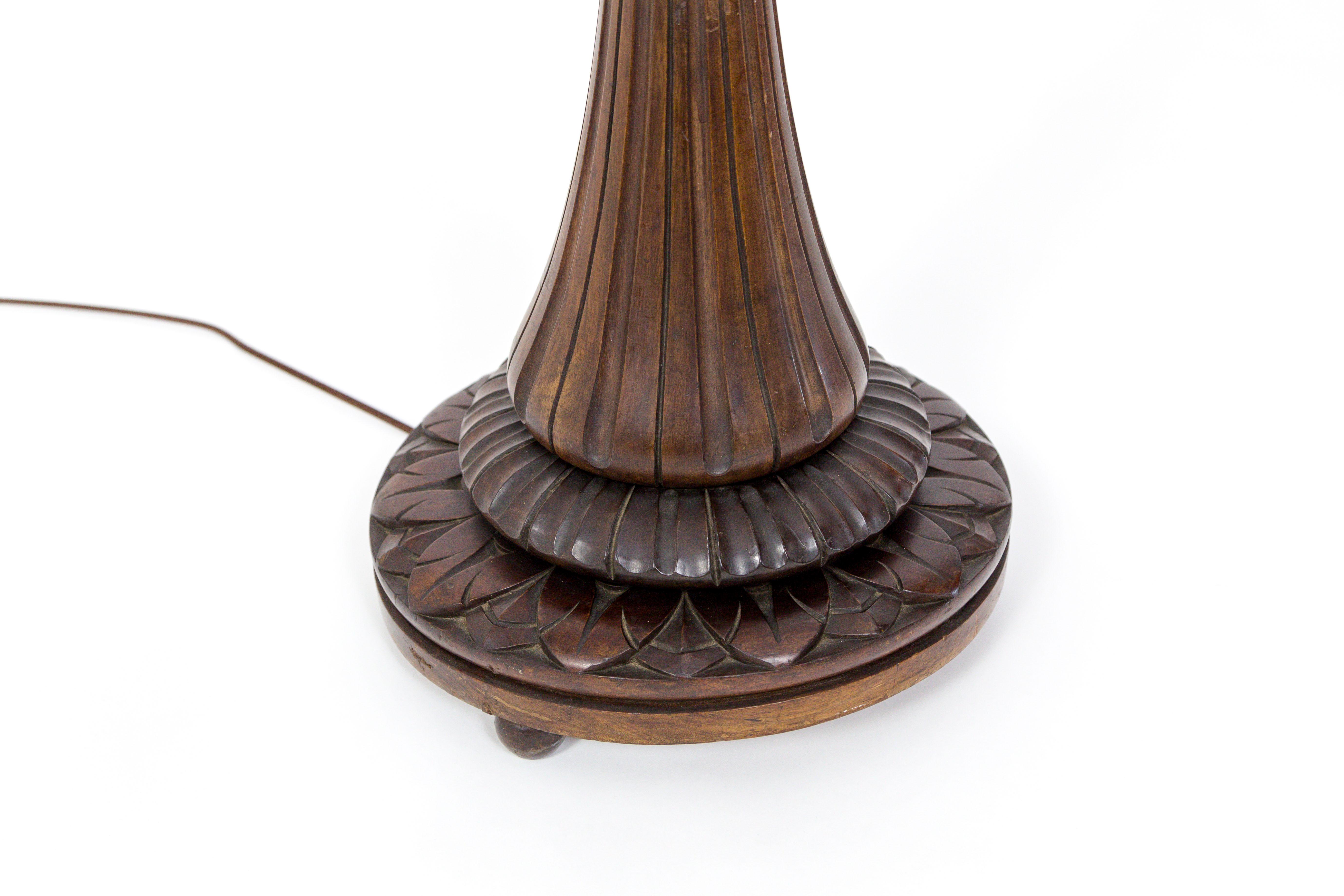 A beautiful carved, monumental, fluted, mahogany floor lamp, with leaf details at the base and gadrooned and floral accents on the stem. With three, disk shaped feet, and brown, fabric covered cord. Arts and Crafts movement; England, circa 1920s.