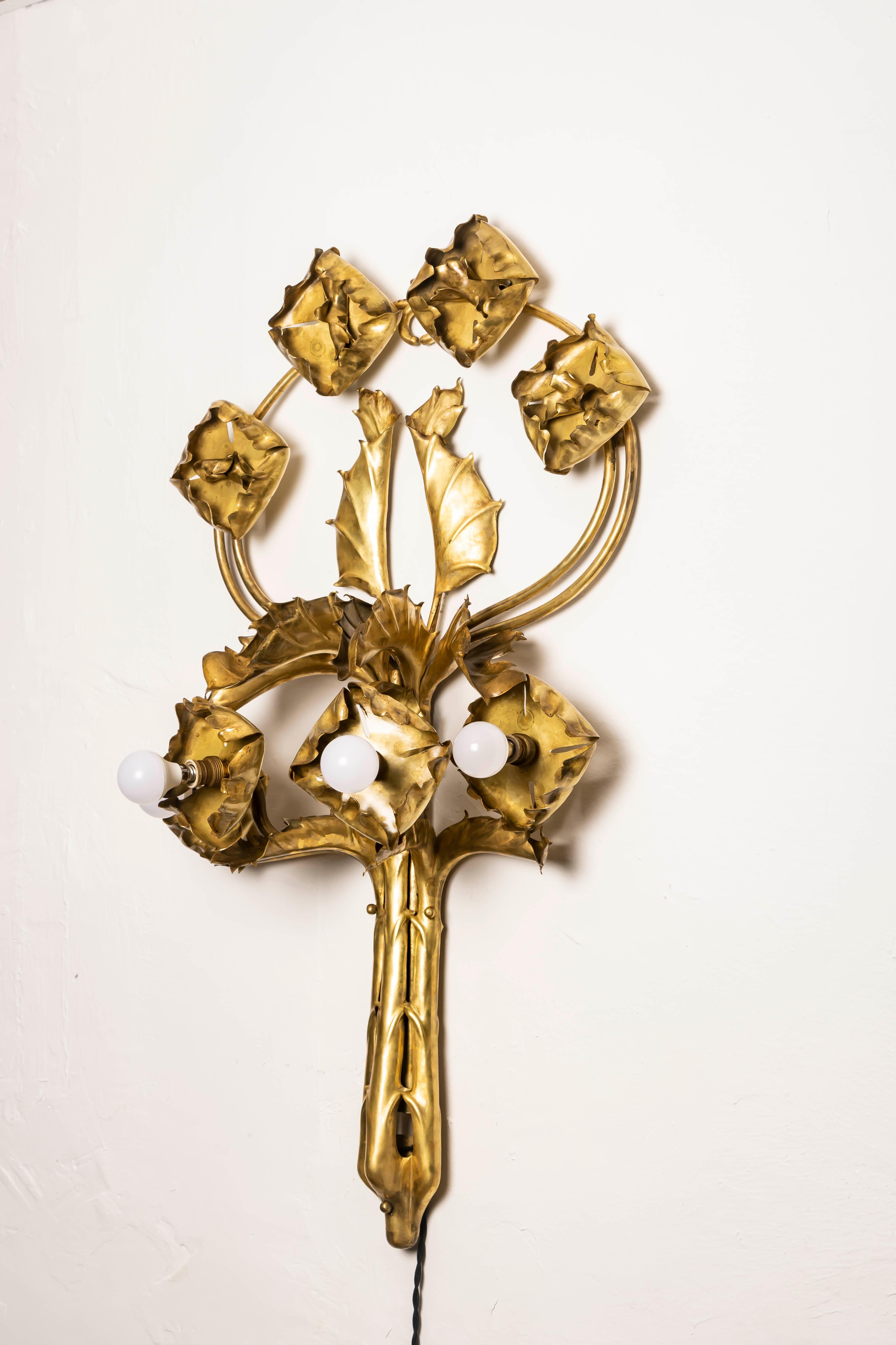 Monumentale applique francese in ottone martellato a mano (dinanderie), inizio XX secolo. Il design traduce il motivo simbolista del cardo e del fiore in una scultura in metallo: foglie stratificate e ripassate e calici arricciati si ergono lungo