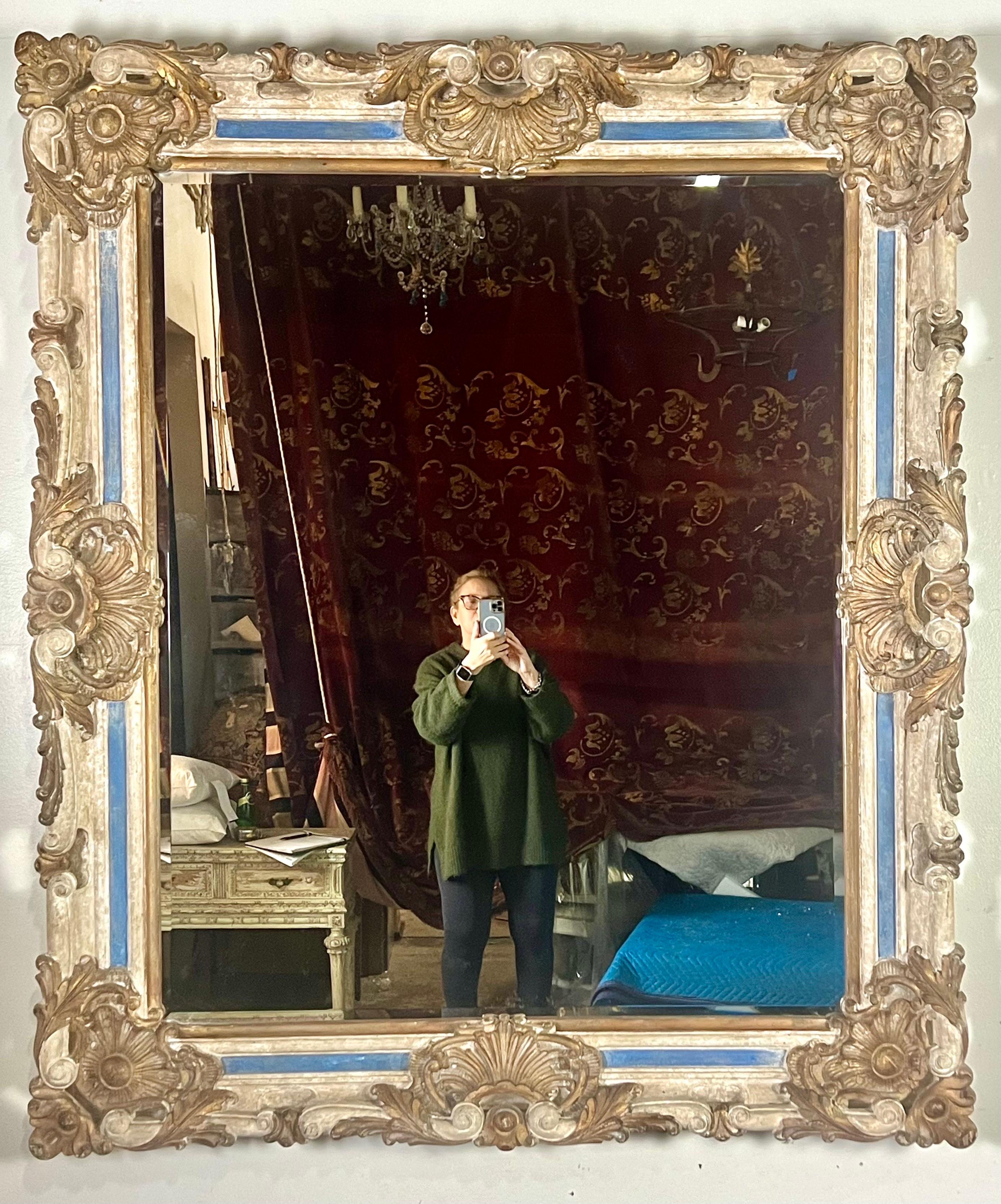 Uno specchio monumentale in stile barocco francese, un capolavoro di design e artigianato che cattura l'opulenza e la grandezza di un'epoca passata.  Questo squisito pezzo è pesantemente intagliato e presenta una serie di elementi decorativi che