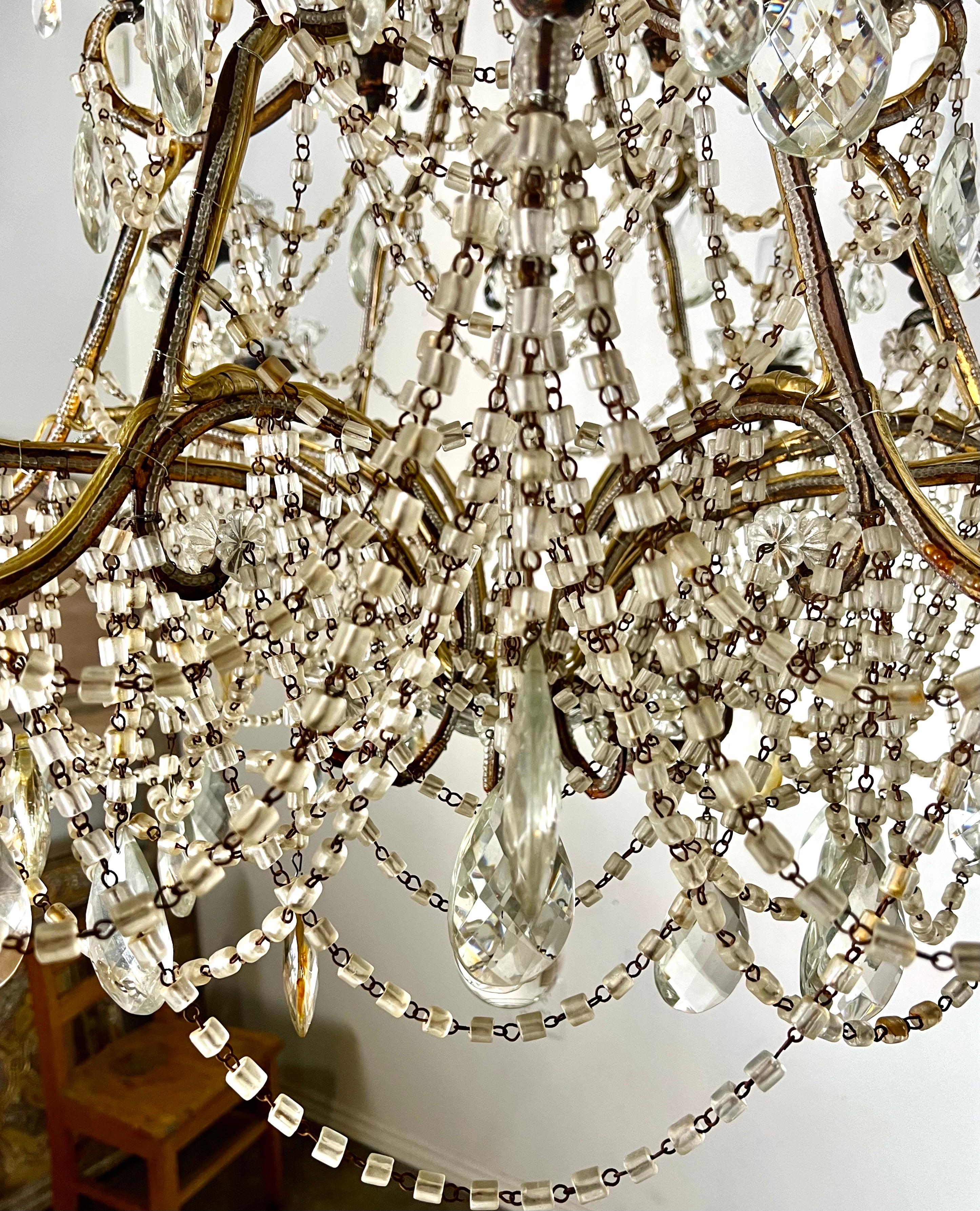 Monumental French ornate chandelier featuring (18) lights with drip wax candle covers.  The design is elaborate and detailed, featuring macaroni style beads and almond shaped crystal.    The opulence and grandeur was typical of the Rococo period. 