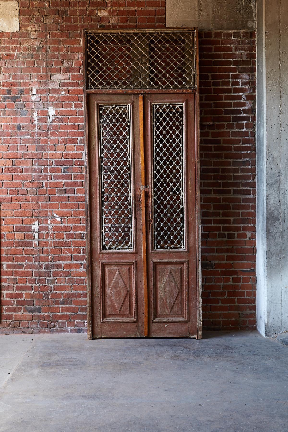 Monumental pair of 19th century French entry doors and transom mounted in a frame. Featuring solid cast iron grills with Moorish style geometric decorative patterns. Handsome relief wood panels and door trim. There is a newer piece of wood running