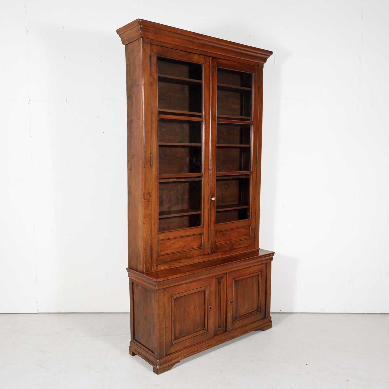 A monumental French Louis Philippe period Lyonnaise bibliotheque or bookcase handcrafted of solid walnut by skilled craftsman in Lyon, circa 1840s. The upper bookcase has a moulded cornice over the original hand blown glass paned locking doors and