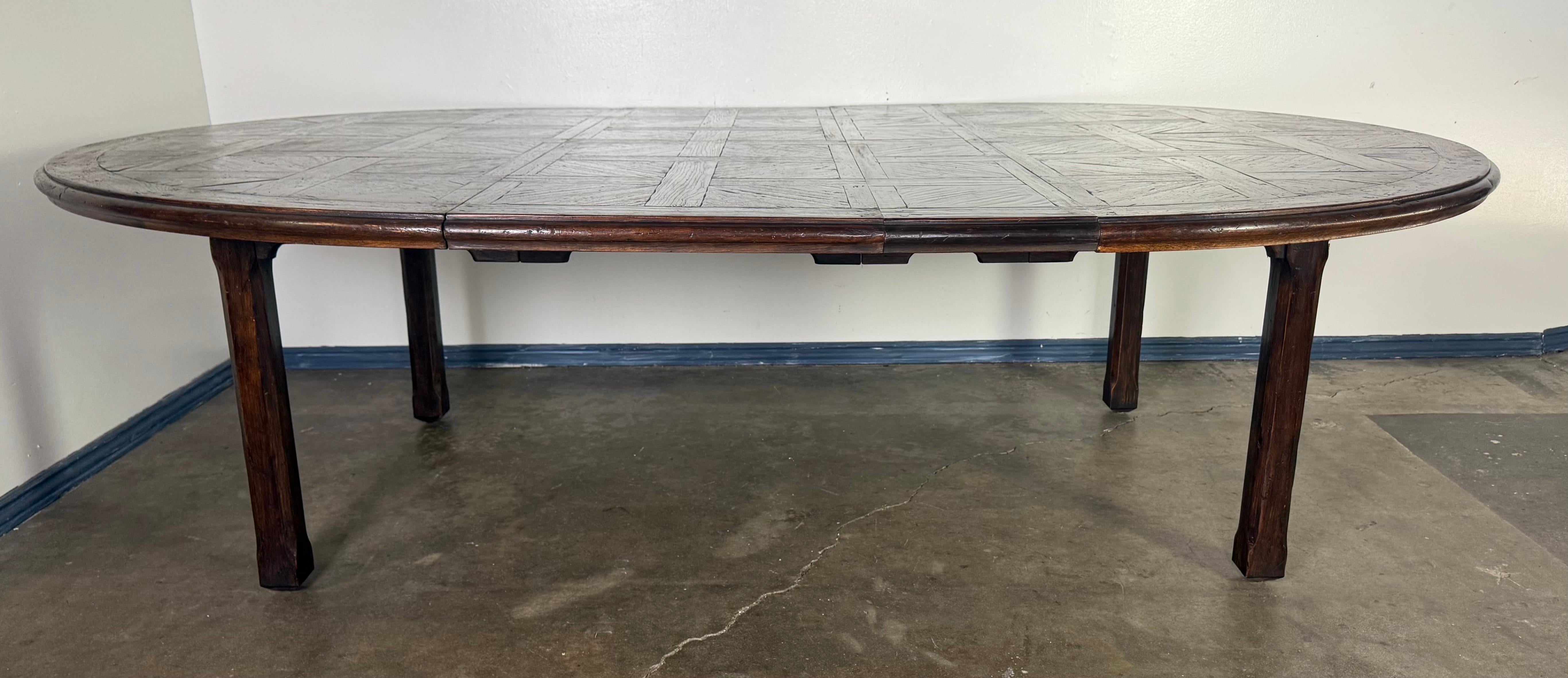Se trata de una mesa de comedor redonda vintage de 70 pulgadas, fabricada con madera teñida en tonos oscuros. El tablero presenta una intrincada incrustación de estilo parqué, dispuesta en un patrón geométrico que añade textura e interés visual. La