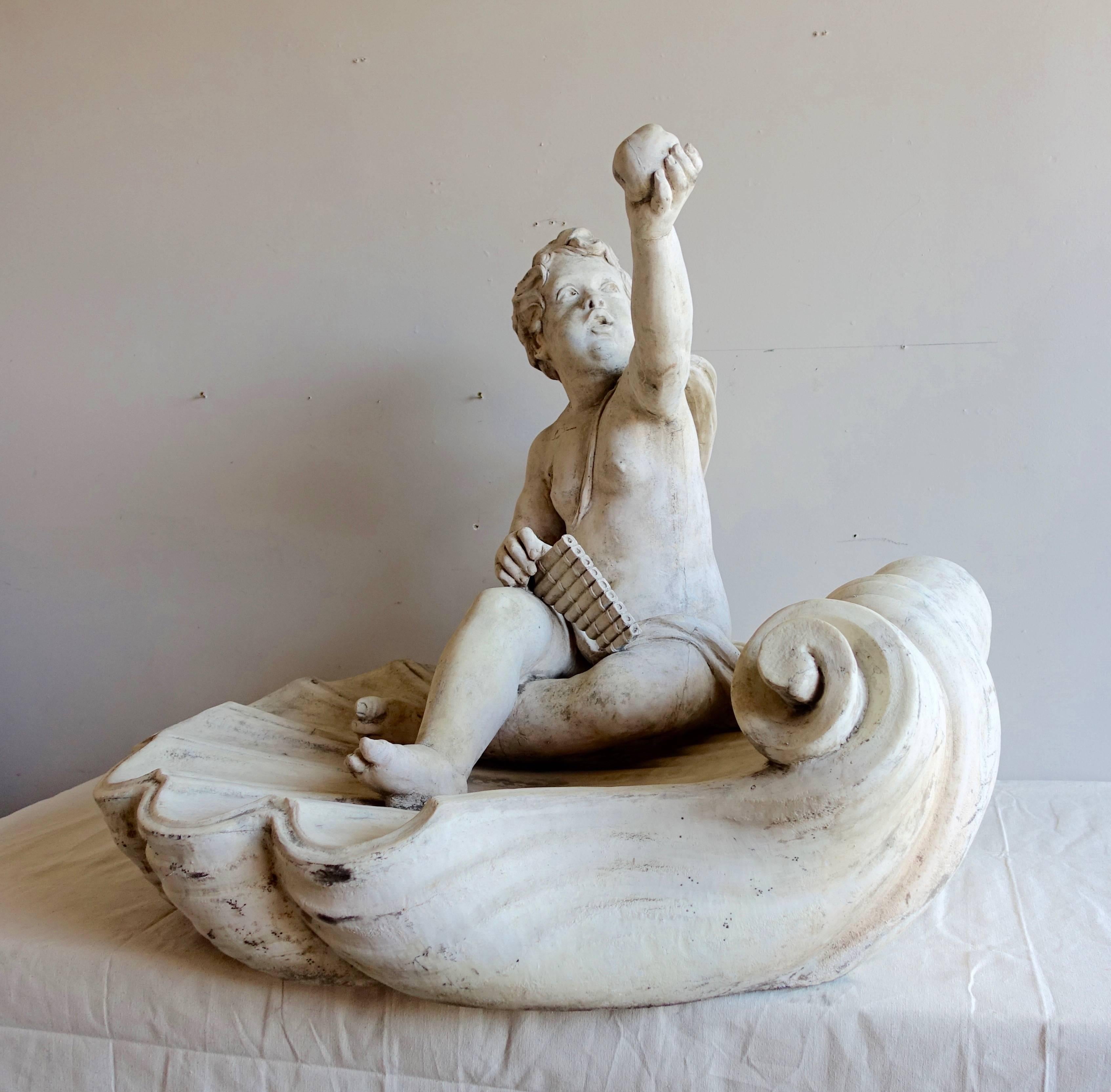 Charming monumental sized cherub sitting on a large shell with a flute and apple in hand. This would look beautiful in a garden.