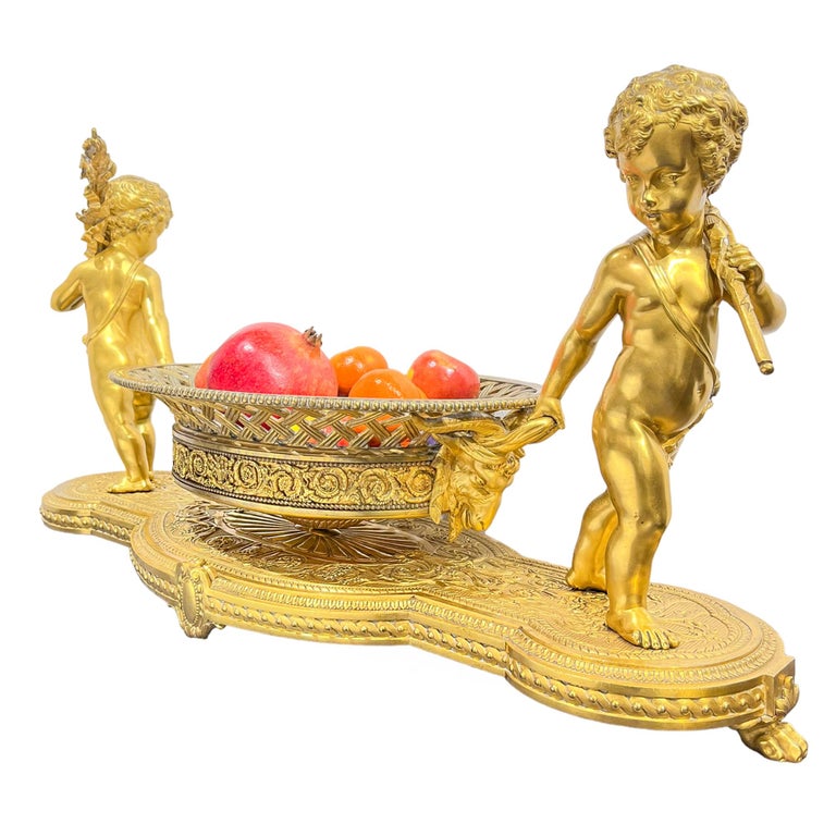 Important gilt bronze centerpiece with each end with a freestanding cherub/putti holding the large, central, reticulated basket by the ram's-head handles; the base raised on paw feet.

Origin: French

Date: circa 1875, late 19th