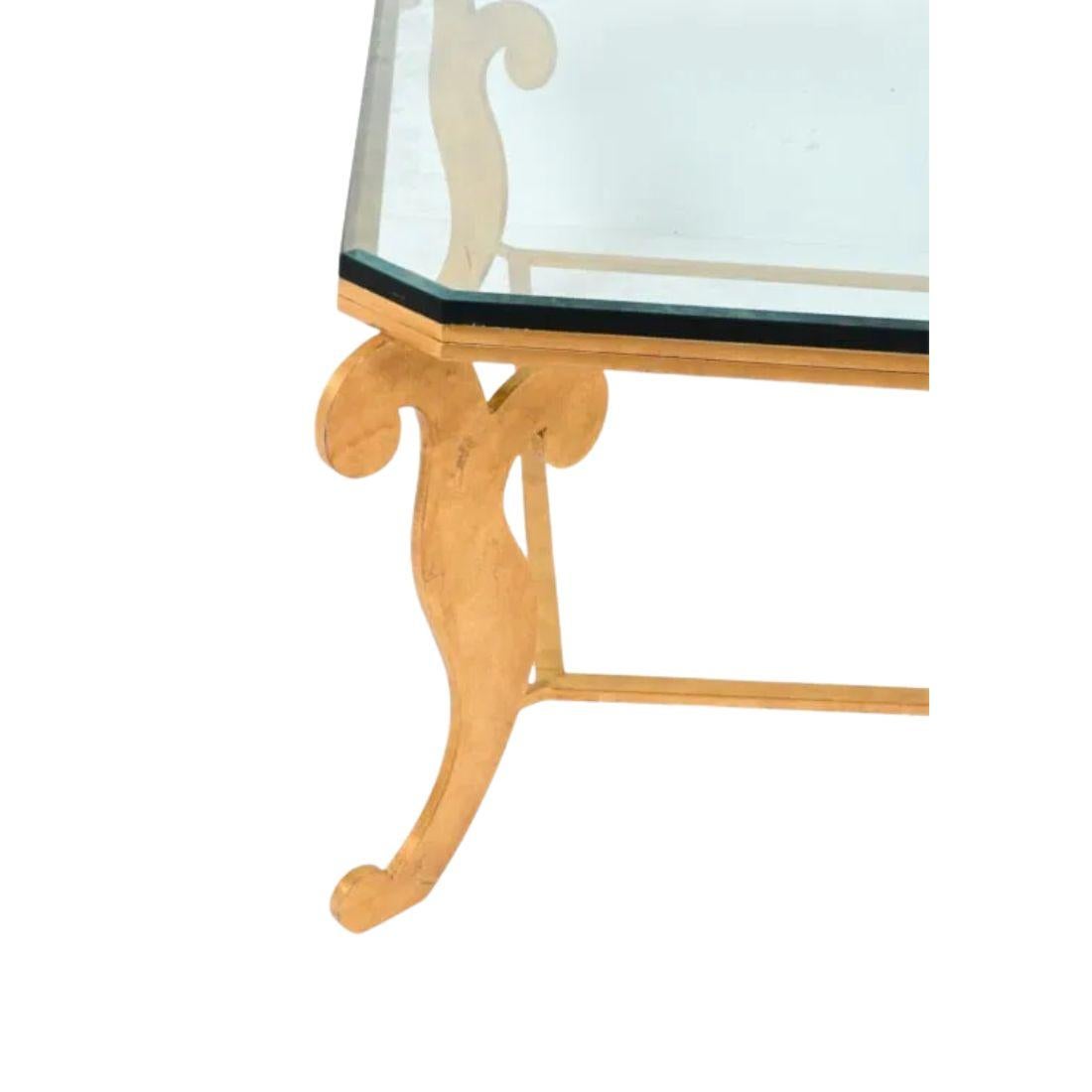 Cette superbe table basse est un magnifique exemple du style Hollywood Regency, avec un grand pied en fer doré qui rayonne de luxe et de sophistication. Le grand cadre présente des détails de volutes sur les pieds, ajoutant une touche de charme
