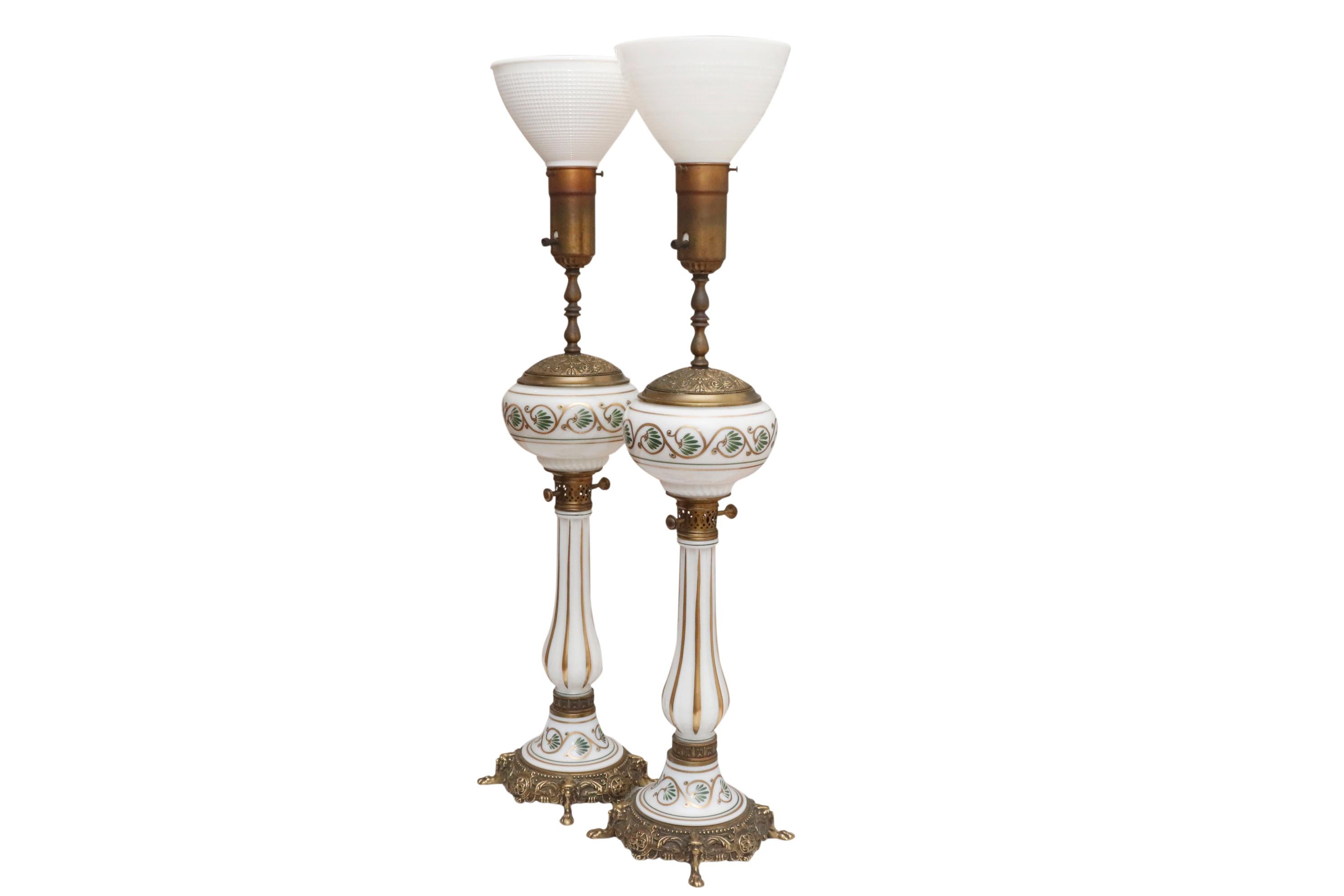 A pair of monumental neoclassical brass and glass uplighter lamps. Torchiere milk glass shades sit on turned brass columns above richly pressed vase tops. Glass vases are hand painted with a simple gold scroll with leaf motif repeated above brass